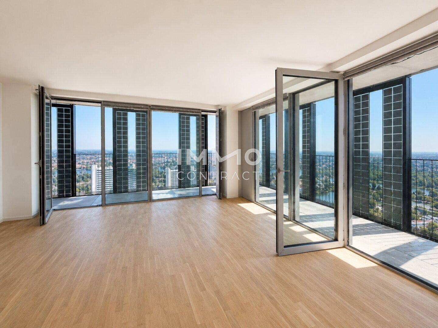 Geräumiges Wohnzimmer mit Parkettboden und großen Fensterfronten, die viel Tageslicht hereinlassen.