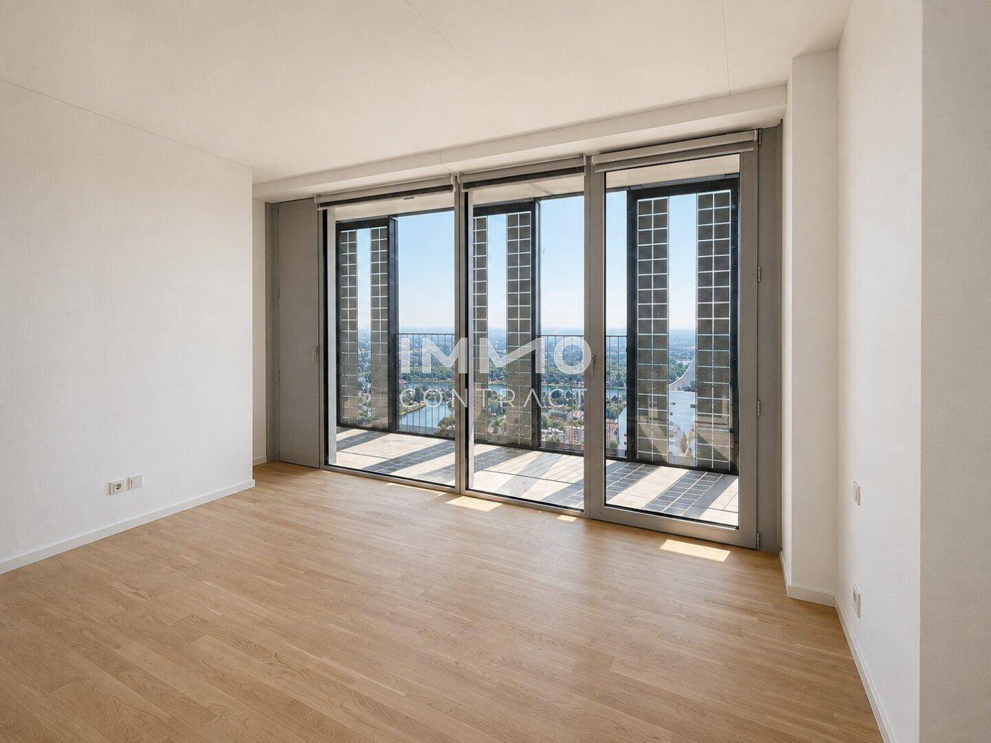 Heller Raum mit Holzboden und großen Fenstern, die einen weiten Blick über die Stadt ermöglichen.