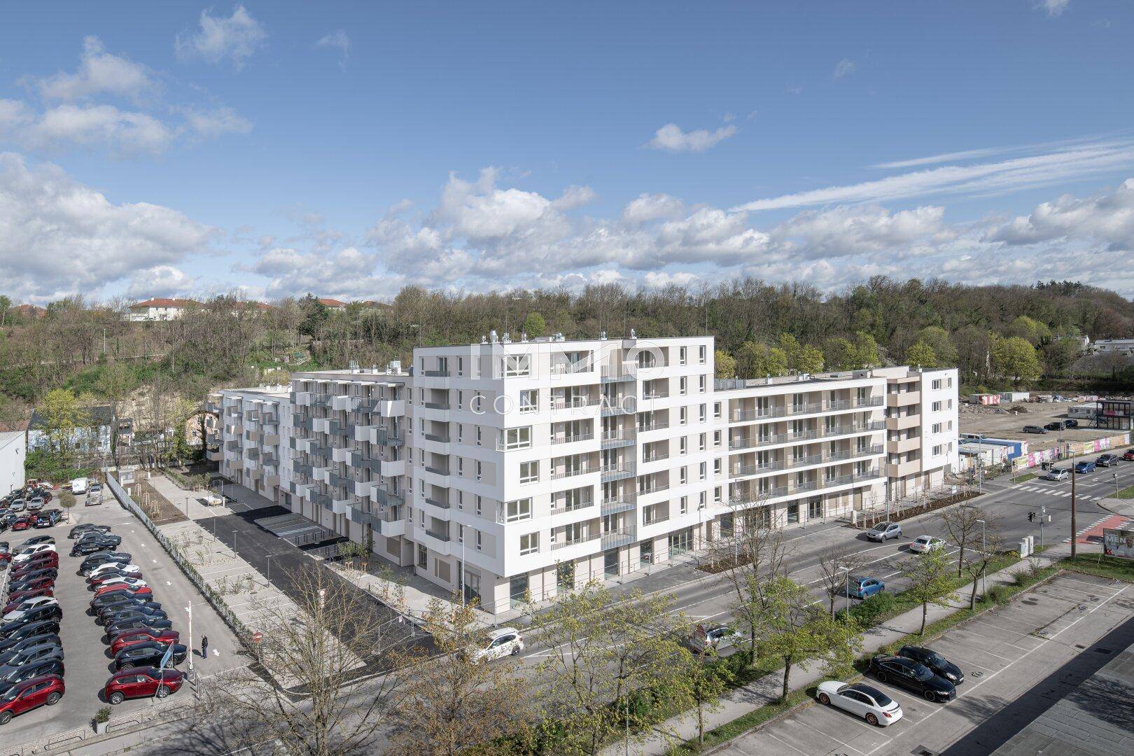 Weitläufige Ansicht eines modernen Wohnkomplexes mit vielen Parkplätzen und umgebender Natur.
