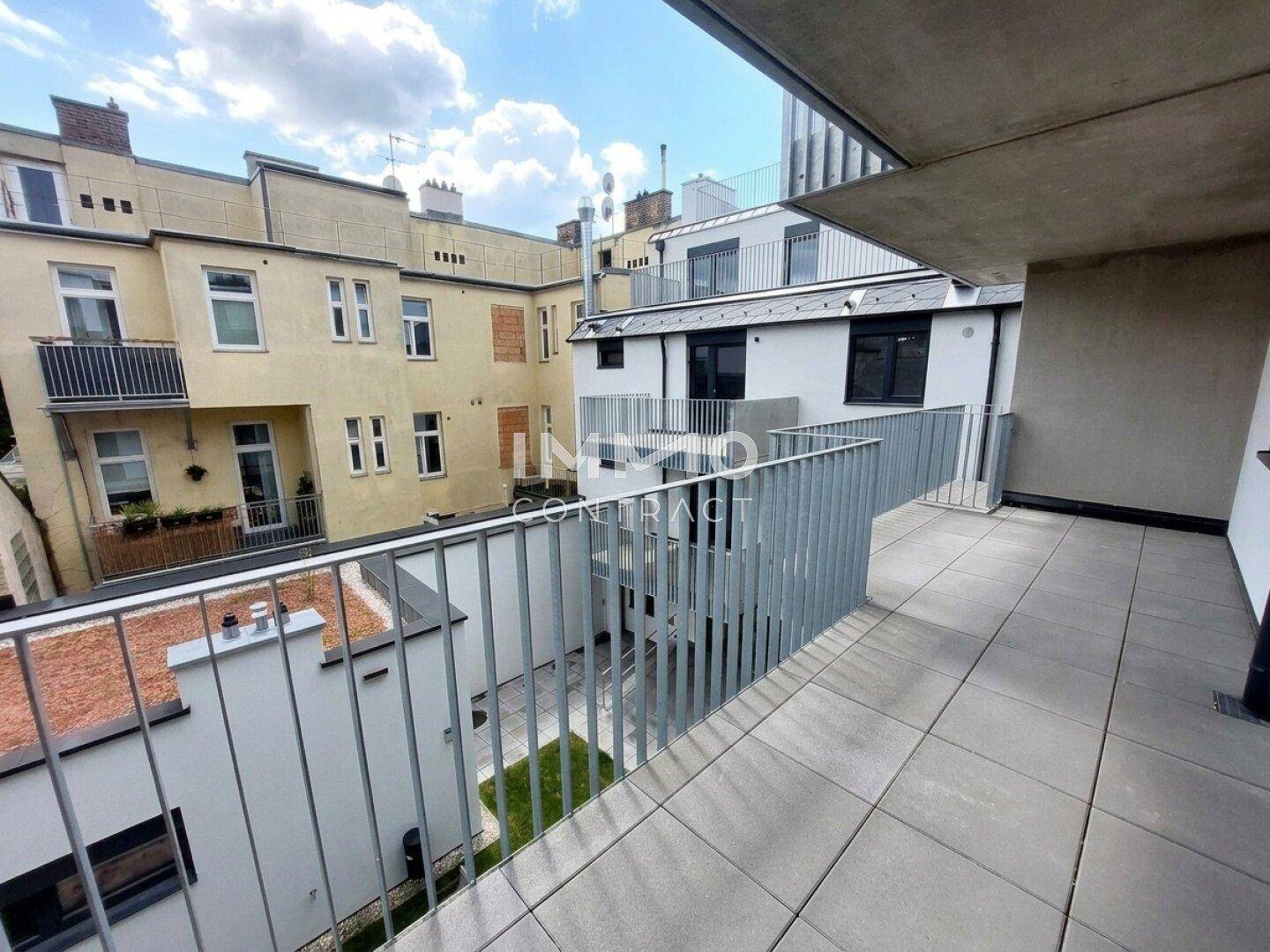 Balkon mit Blick auf den Innenhof und die umliegenden Wohngebäude bei sonnigem Wetter.