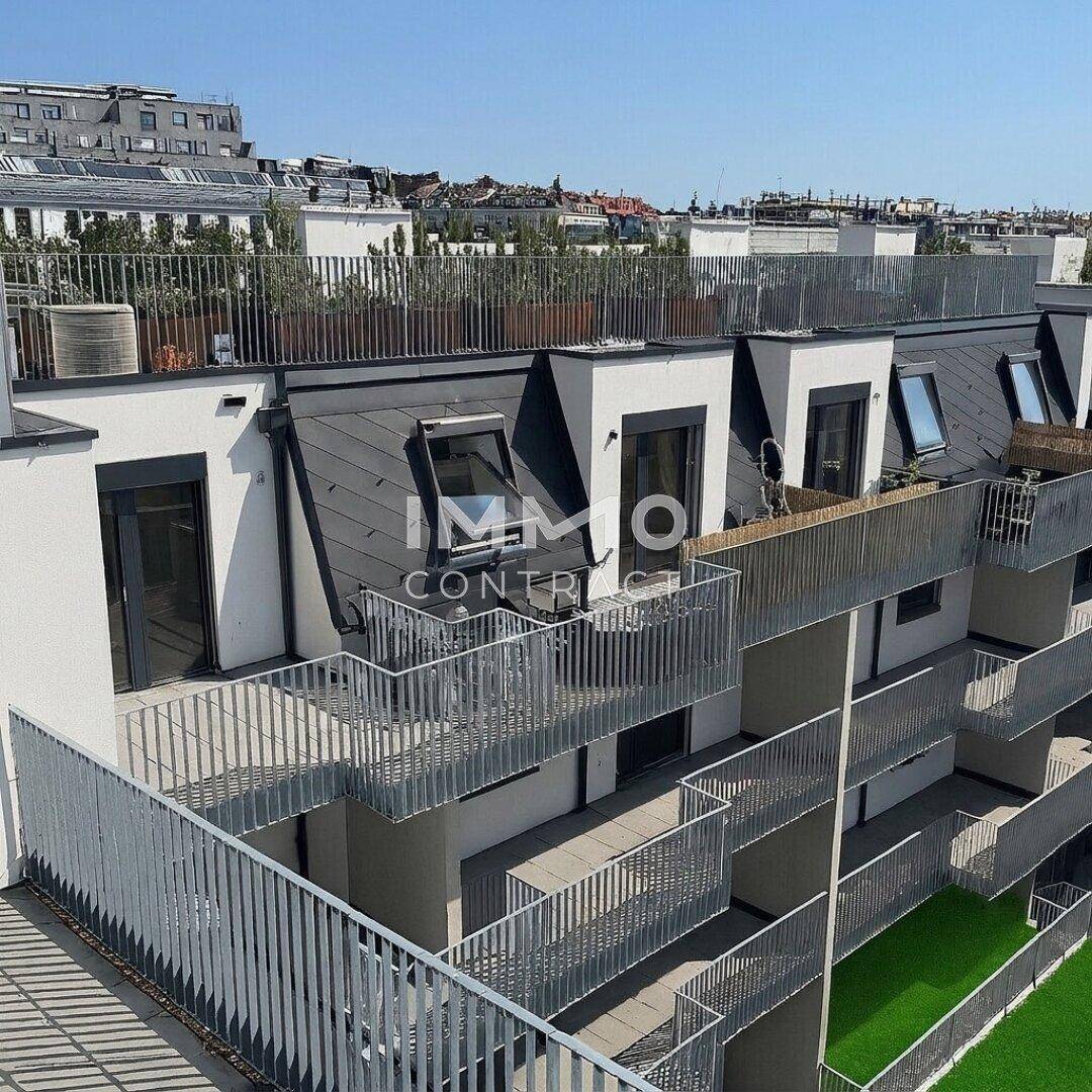 Moderne Gebäudefassade mit mehreren Balkonen, Dachfenstern und Blick auf die Stadt.