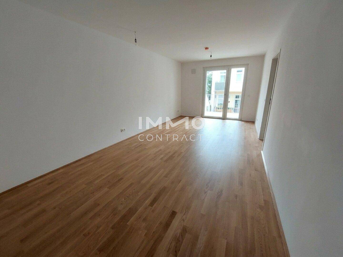 Geräumiges, helles Wohnzimmer mit Holzparkettboden und Zugang zu einem Balkon.