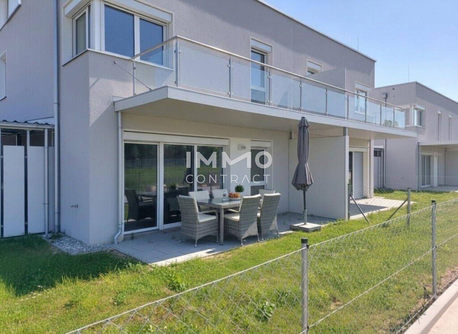 Möblierte Terrasse mit Sonnenschirm und Balkon mit Glasgeländer an der modernen Fassade.