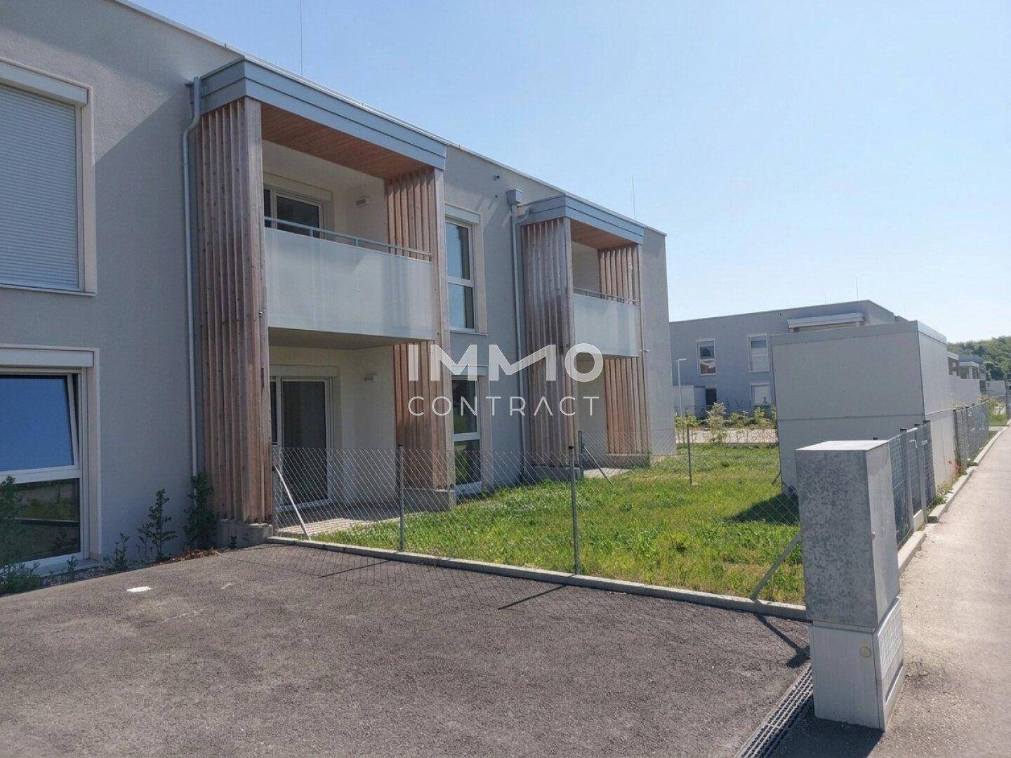 Moderne Wohnanlage mit gepflastertem Vorplatz und Grünflächen unter strahlendem Sonnenschein.