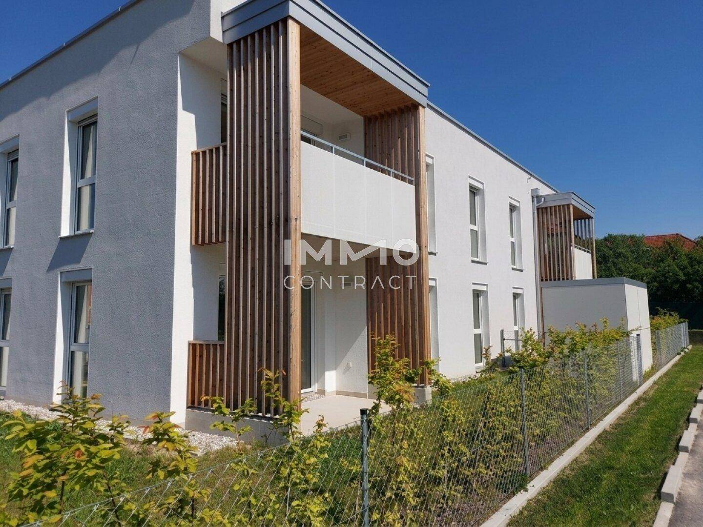 Seitliche Ansicht der modernen Wohnanlage mit Holzverkleidung und Balkonen unter blauem Himmel.
