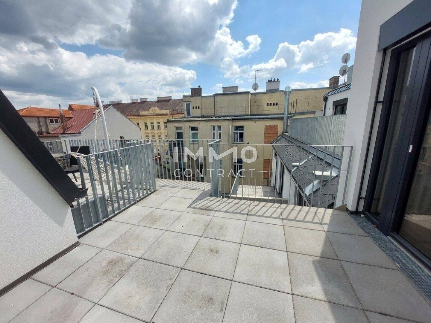Große Dachterrasse mit Fliesenboden, Metallgeländer und Blick auf die umliegenden Gebäude.