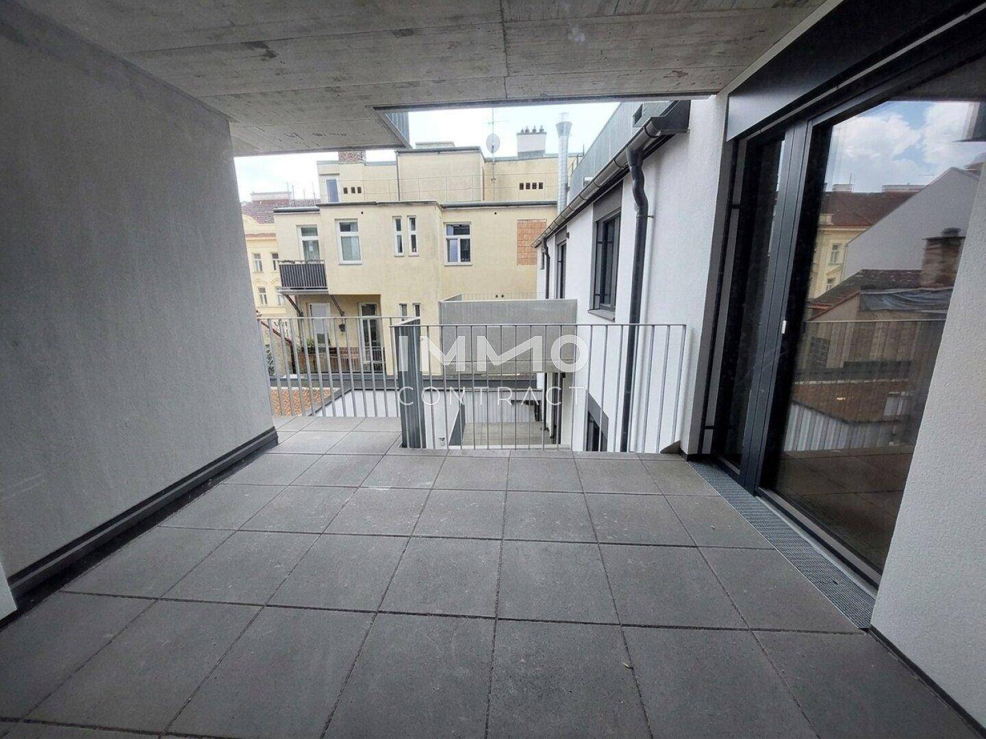 Geräumiger Balkon mit Fliesenboden und moderner Metallbrüstung, umgeben von Stadtgebäuden.