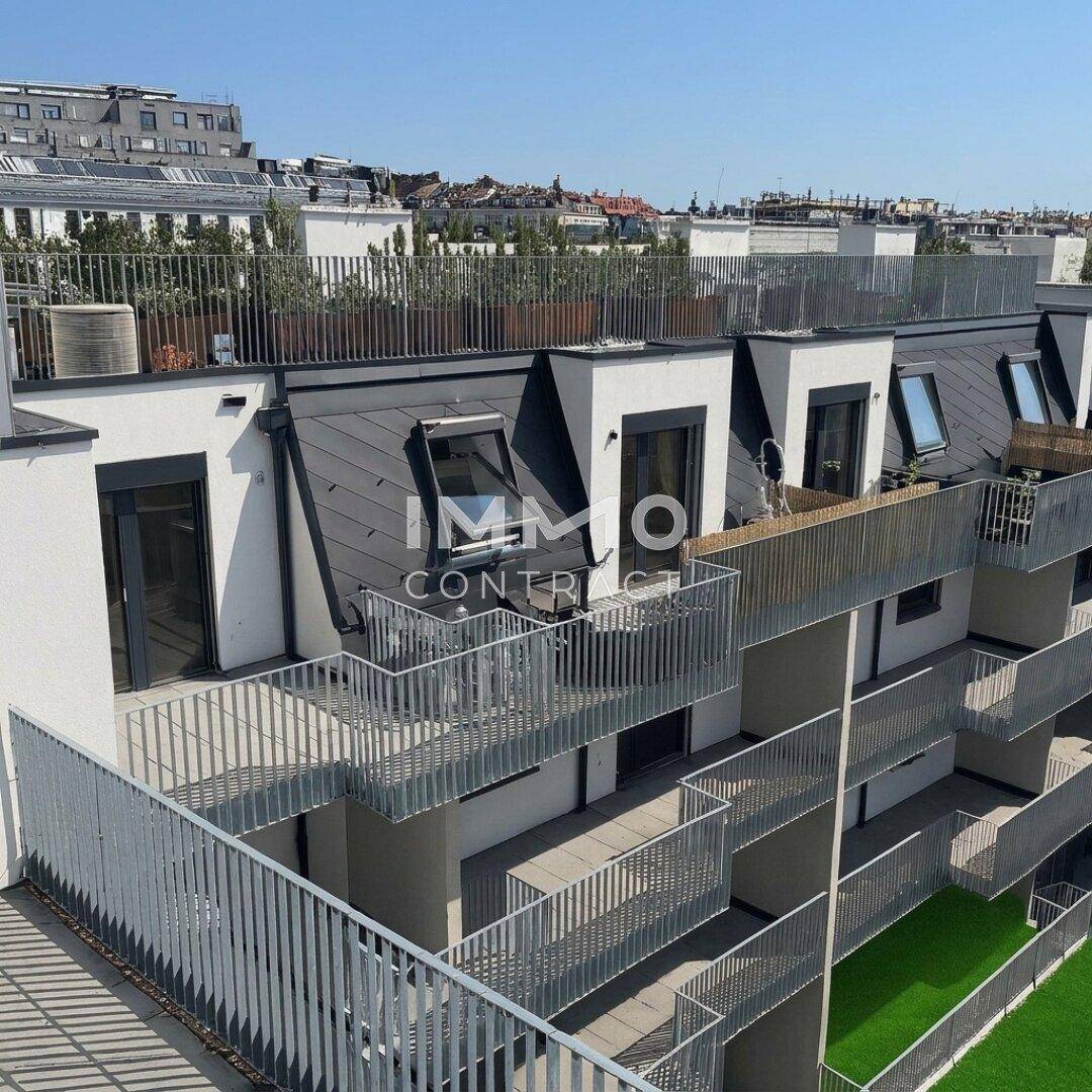 Moderne Wohnanlage mit mehreren Balkonen, Dachterrassen und Dachfenstern unter blauem Himmel.