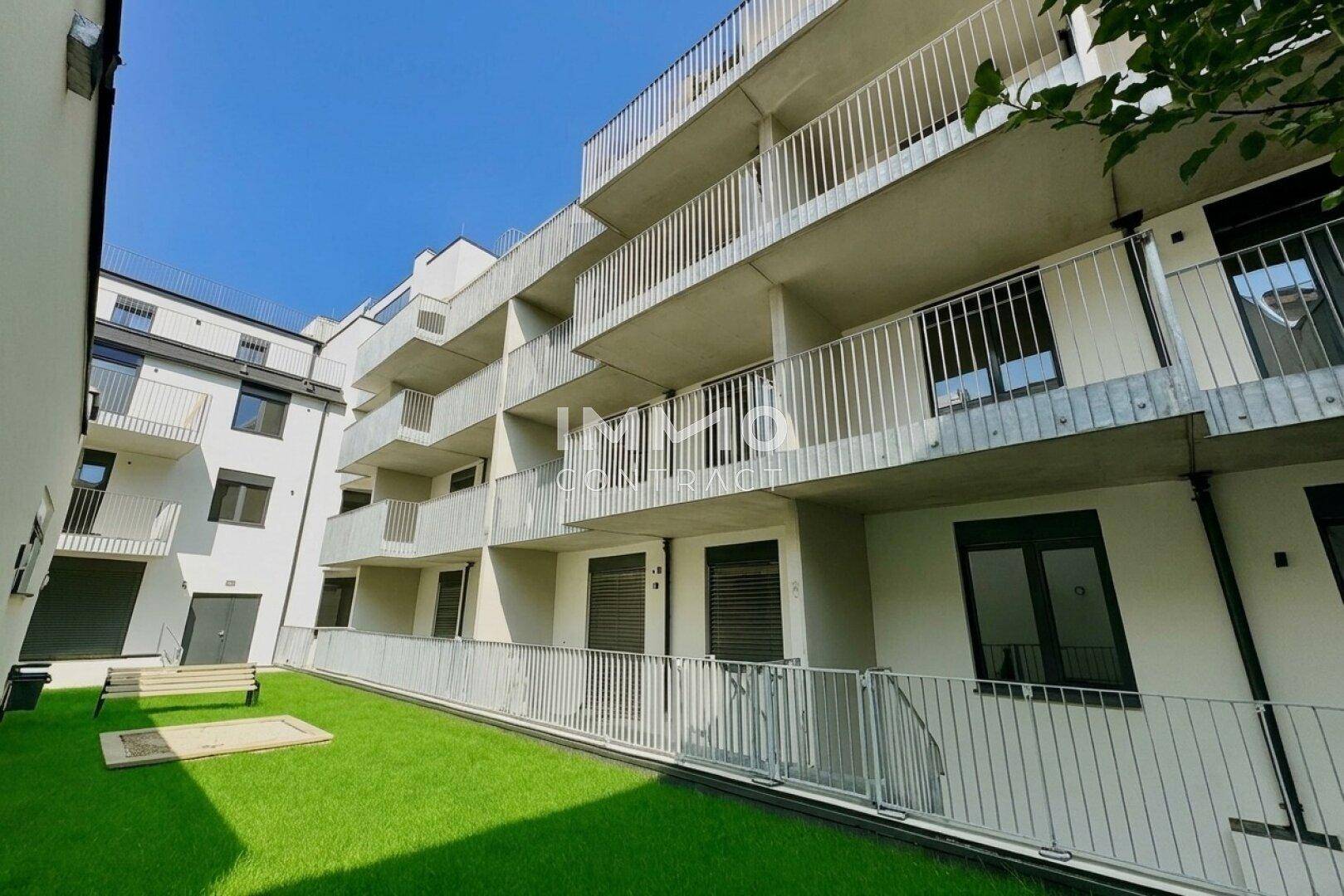 Moderne Wohnfassade mit zahlreichen Balkonen und einer gepflegten Rasenfläche im Erdgeschoss.