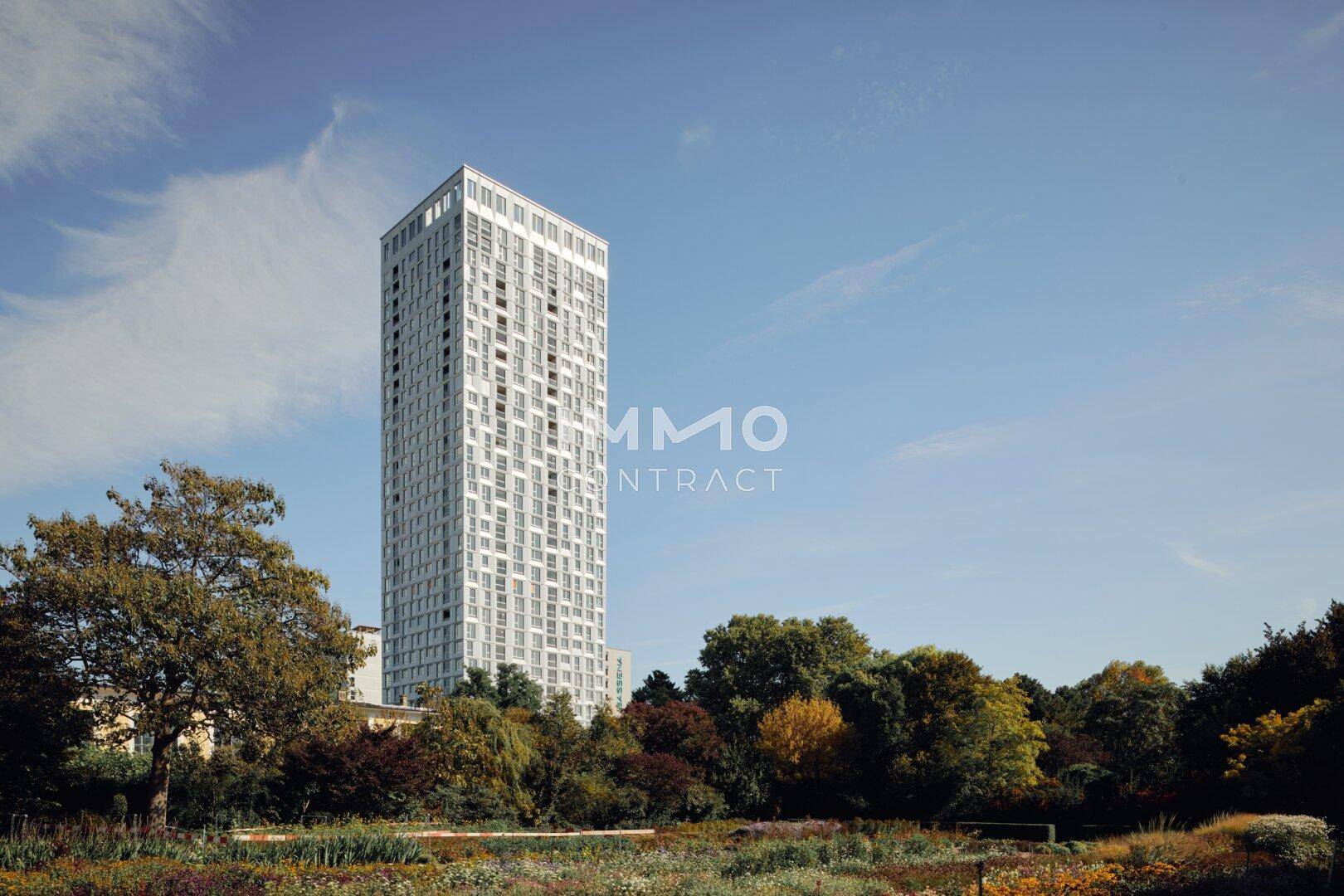 Modernes Hochhaus inmitten einer grünen Parklandschaft unter blauem Himmel.