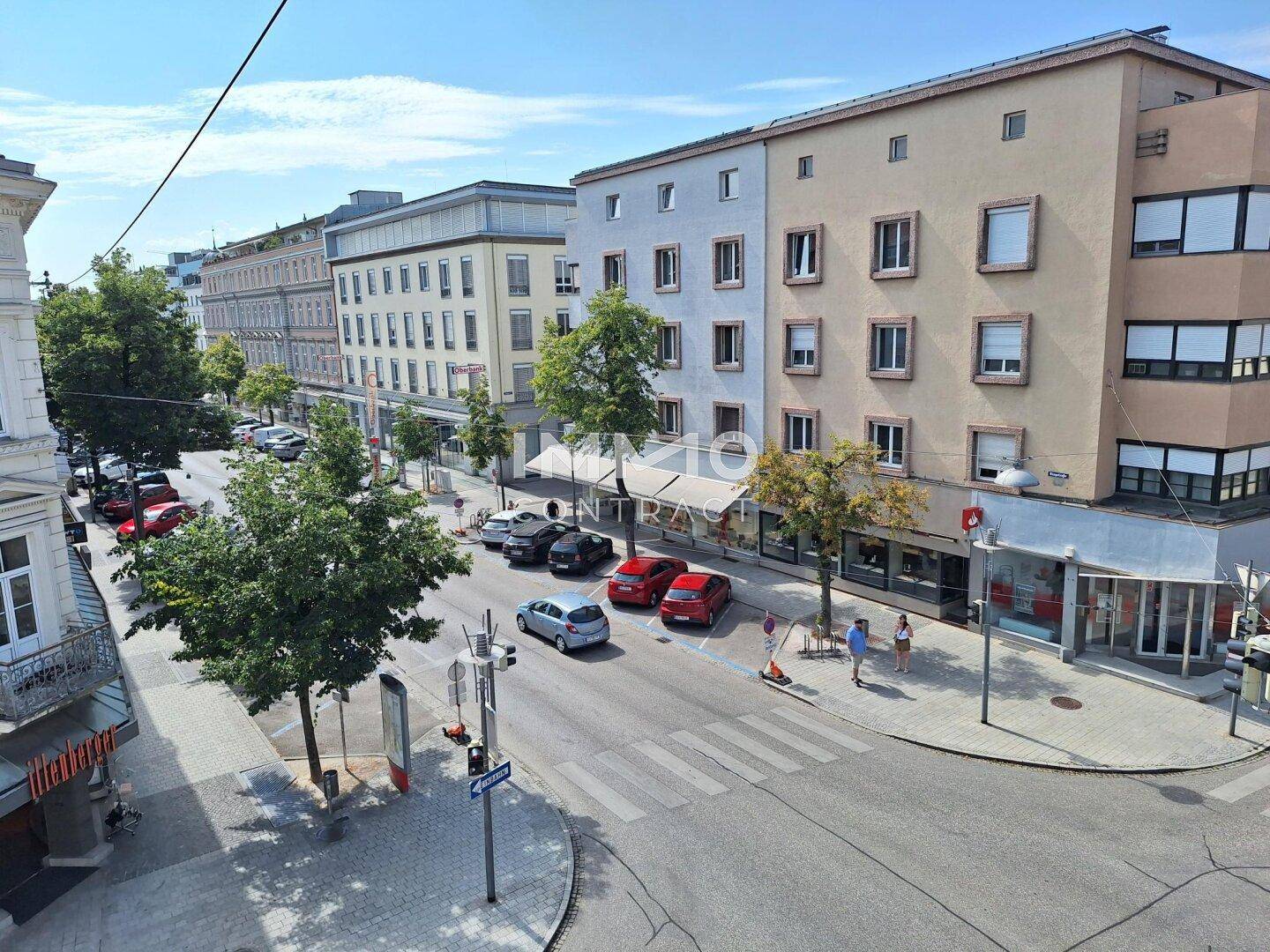 Blick von oben auf eine belebte Stadtstraße mit parkenden Autos und Gebäuden.