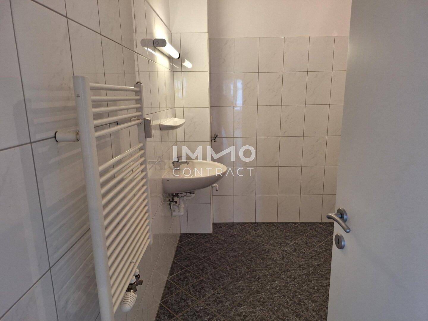 Weiterer Blick in das geflieste Badezimmer mit Waschbecken und praktischem Handtuchheizkörper.