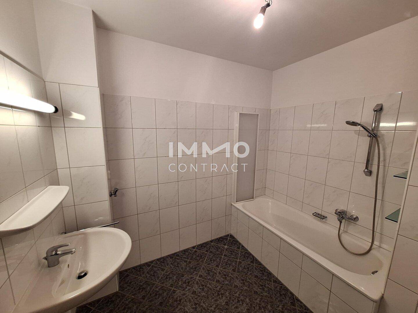 Gefliestes Badezimmer mit Waschbecken und Badewanne inklusive Duschfunktion.