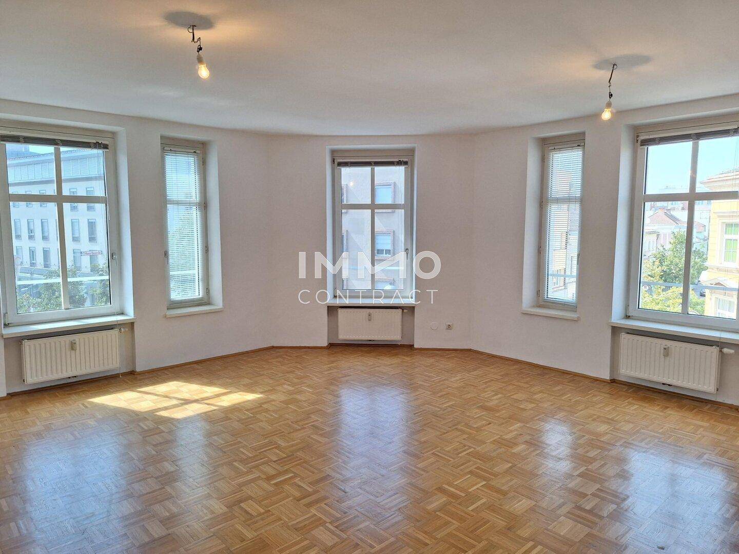 Geräumiges, leeres Zimmer mit Fischgrätparkett und vielen Fenstern, ideal für Wohnzwecke.