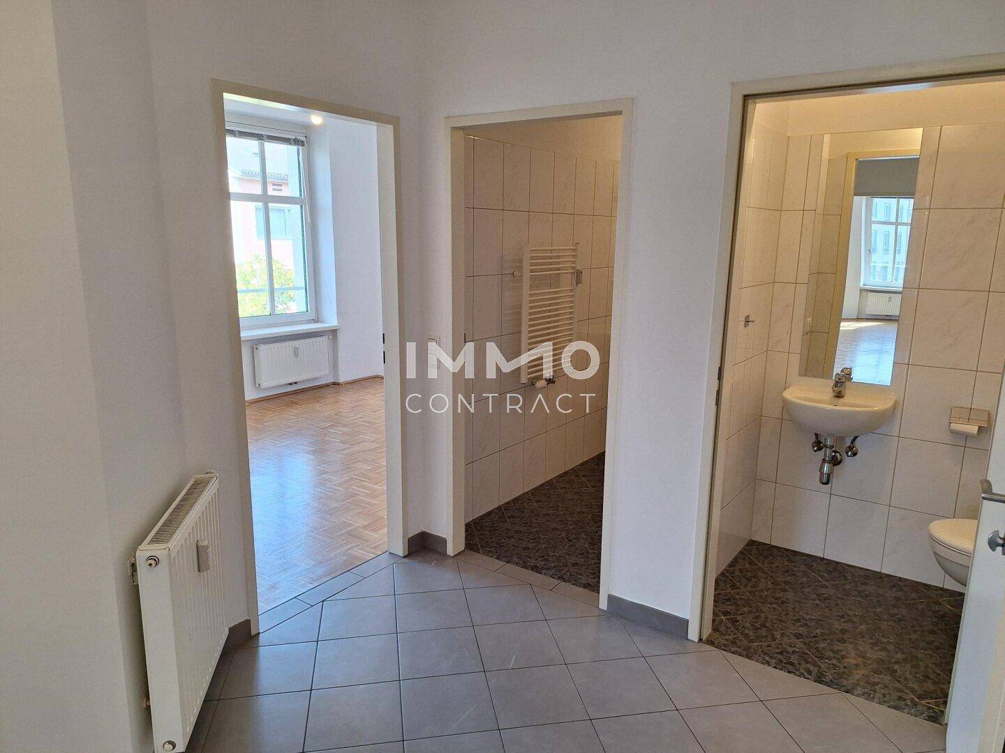 Flur mit Fliesenboden, der zu einem Zimmer und zwei Badezimmern oder WCs führt.