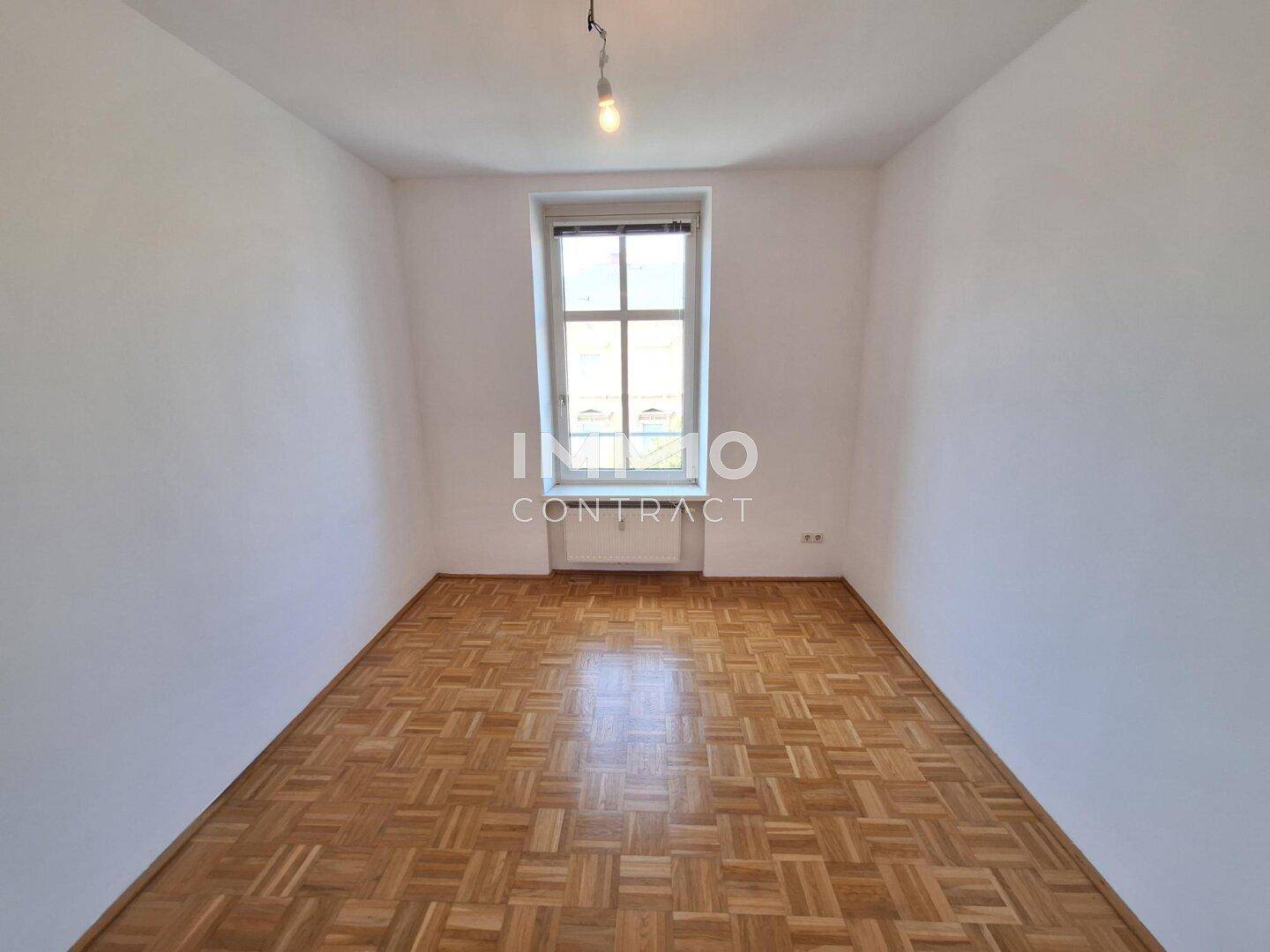 Kleineres, leeres Zimmer mit Fischgrätparkett und einem Fenster, geeignet als Kinder- oder Arbeitszimmer.