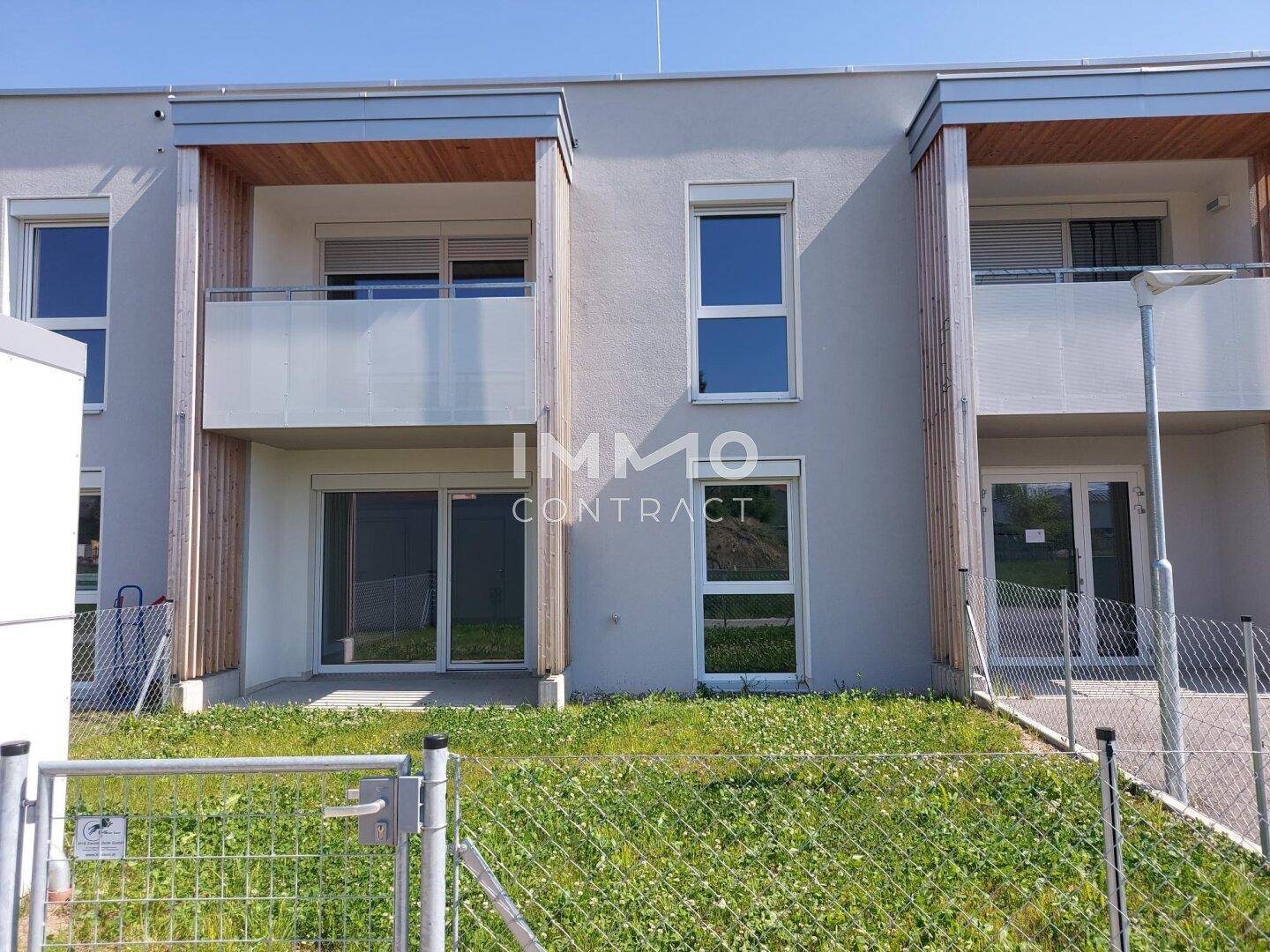Fassade eines modernen Neubaus mit großen Fenstern, Balkonen und Zugang zu ebenerdigen Terrassen.