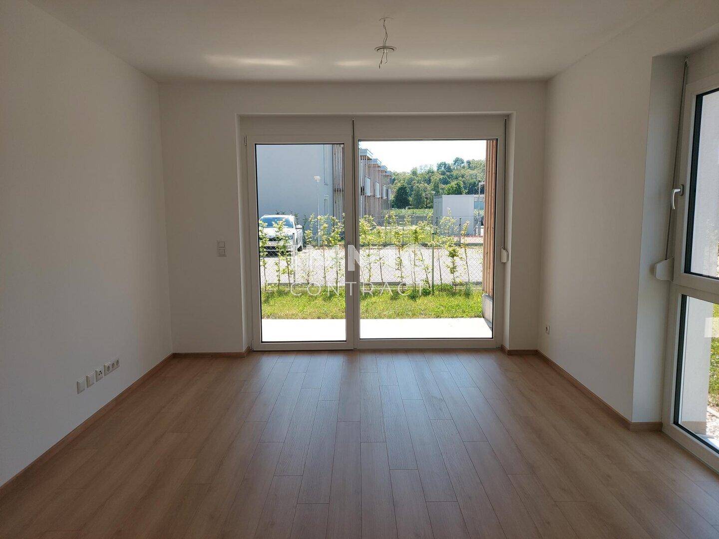 Helles Wohnzimmer mit Laminatboden und großen Glasschiebetüren, die zu einem Außenbereich führen.