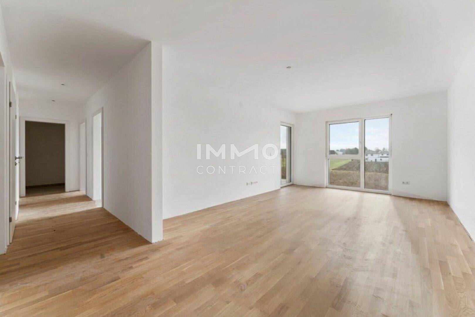 Helles, leeres Wohnzimmer mit Holzboden, weißen Wänden und großen Fenstern.