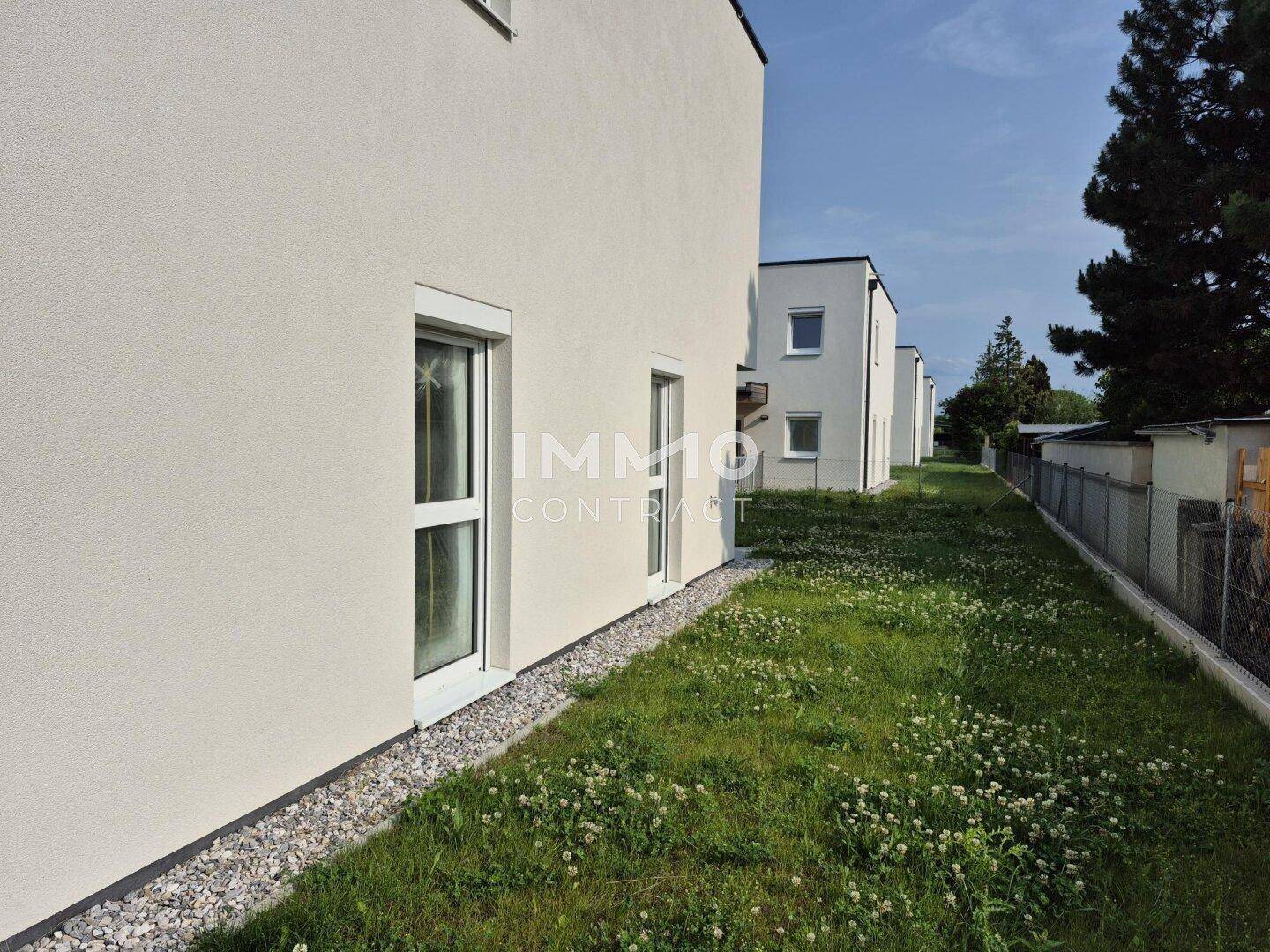 Seitenansicht des Neubaus mit schmalem Grünstreifen und Kiesbett entlang der Fassade.