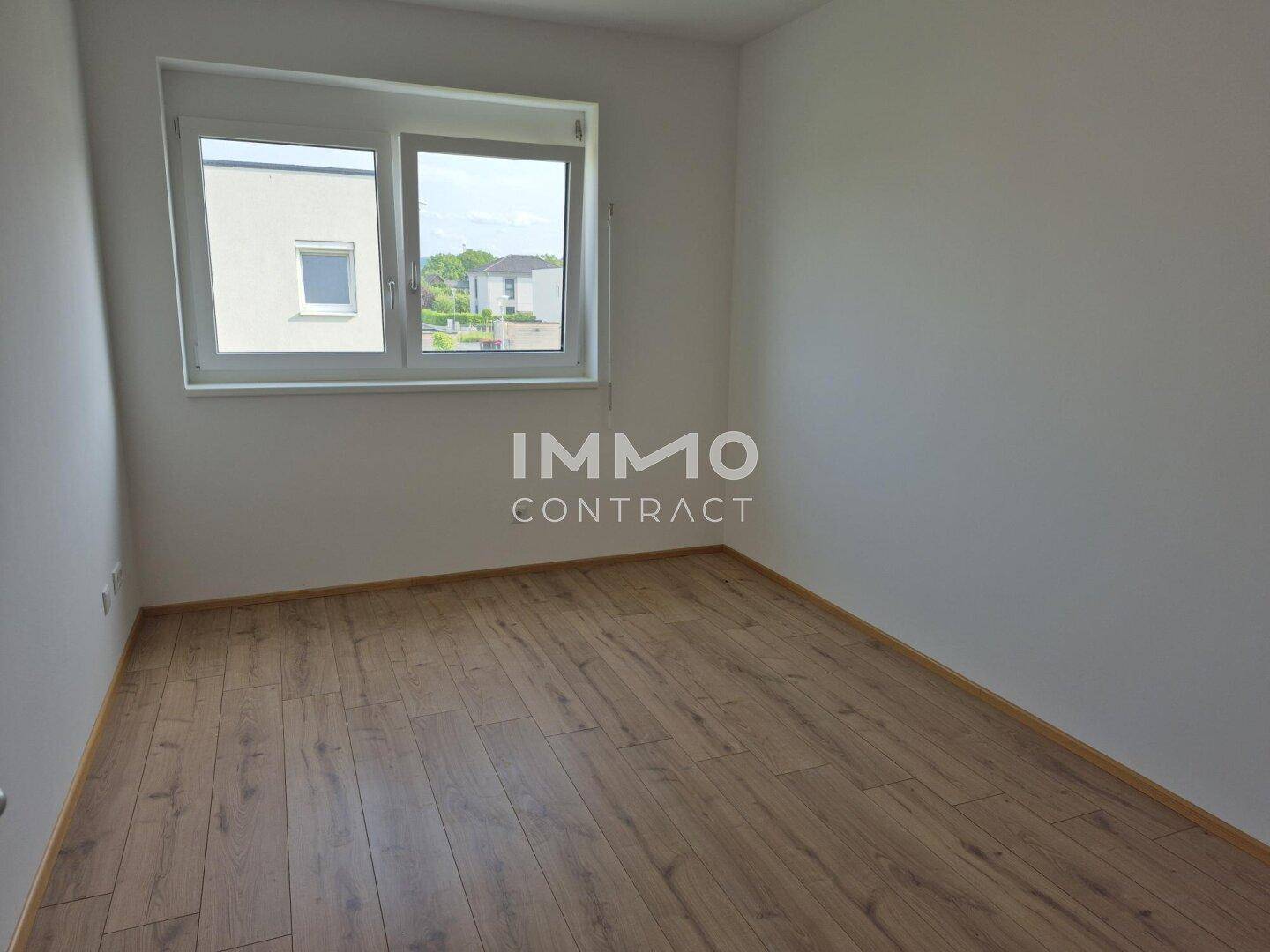 Leeres Schlafzimmer mit großem Fenster, das viel Licht spendet, und hellem Laminatboden.