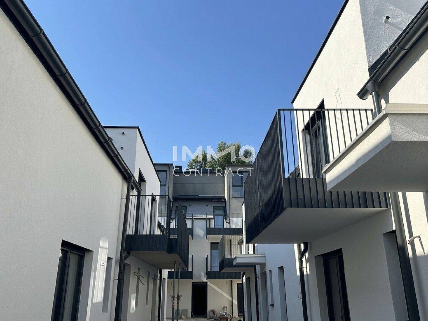 Moderne Wohnanlage mit weißer Fassade, schwarzen Balkonen und klaren architektonischen Linien.