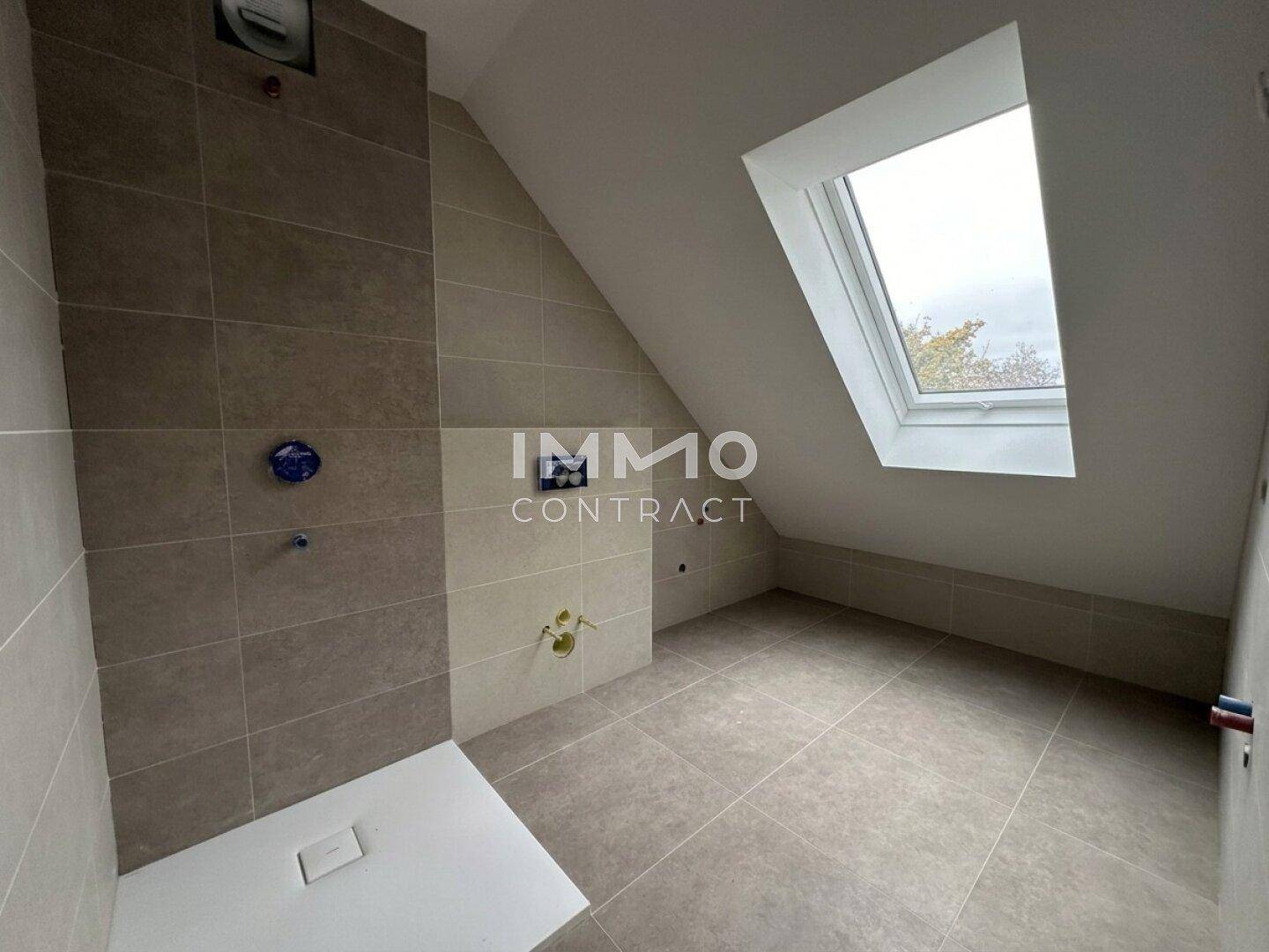 Unfertiges Badezimmer im Dachgeschoss mit Dachfenster und modernen Fliesen an Wänden und Boden.