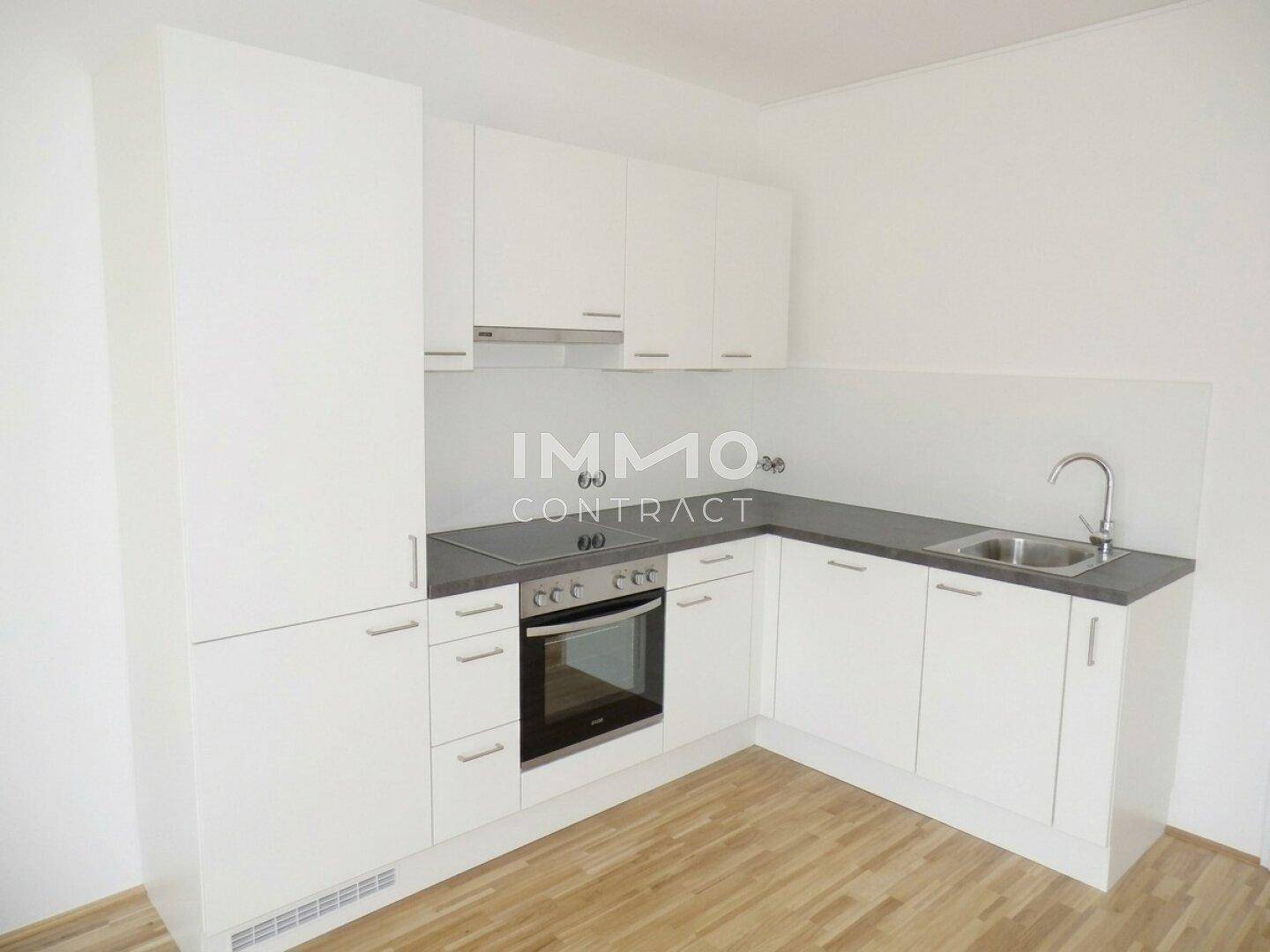 Moderne Einbauküche in Weiß mit Backofen, Kochfeld und Spüle, heller Laminatboden.