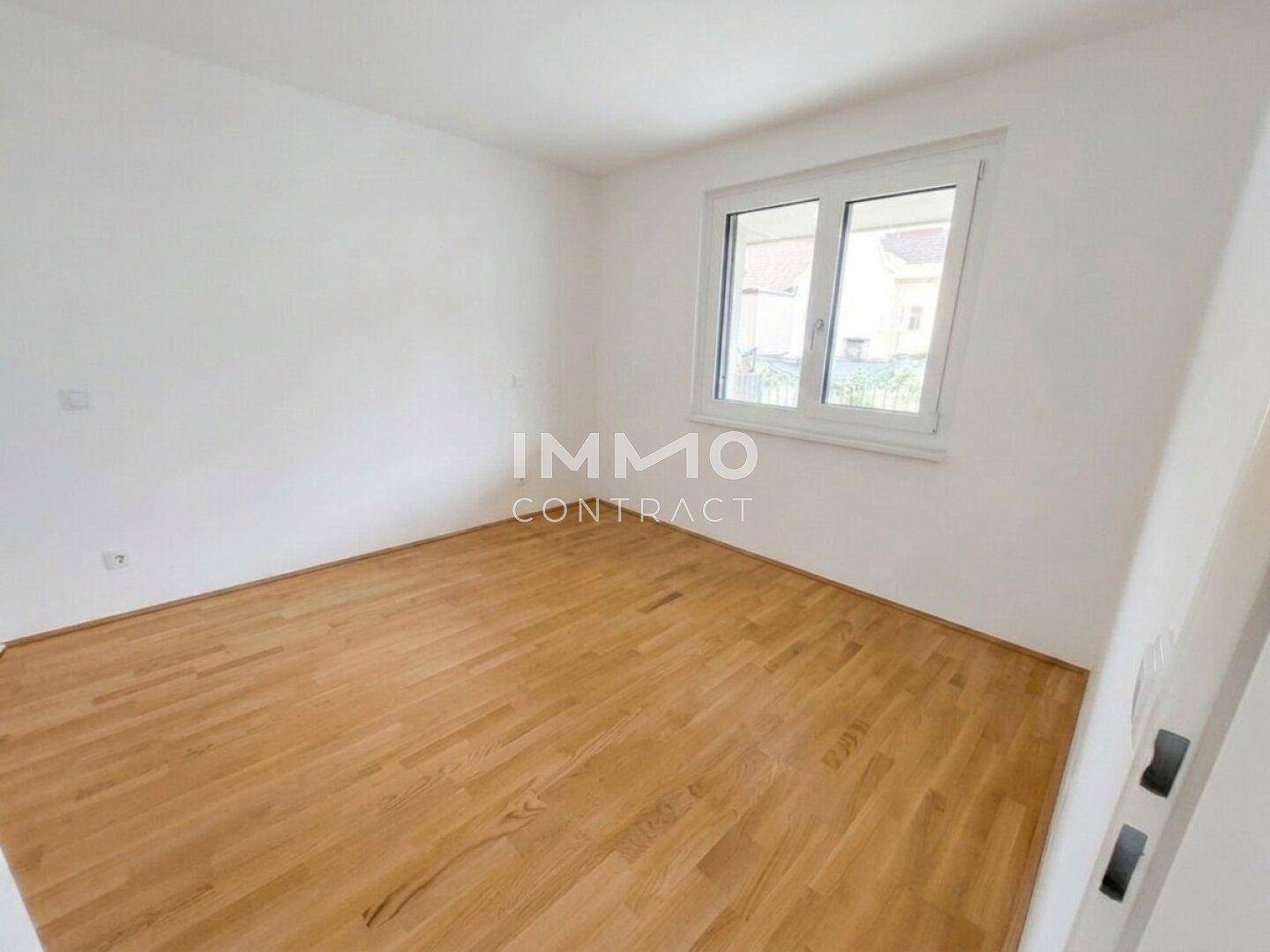 Schlafzimmer mit hellem Holzboden und einem großen Fenster für viel Tageslicht.