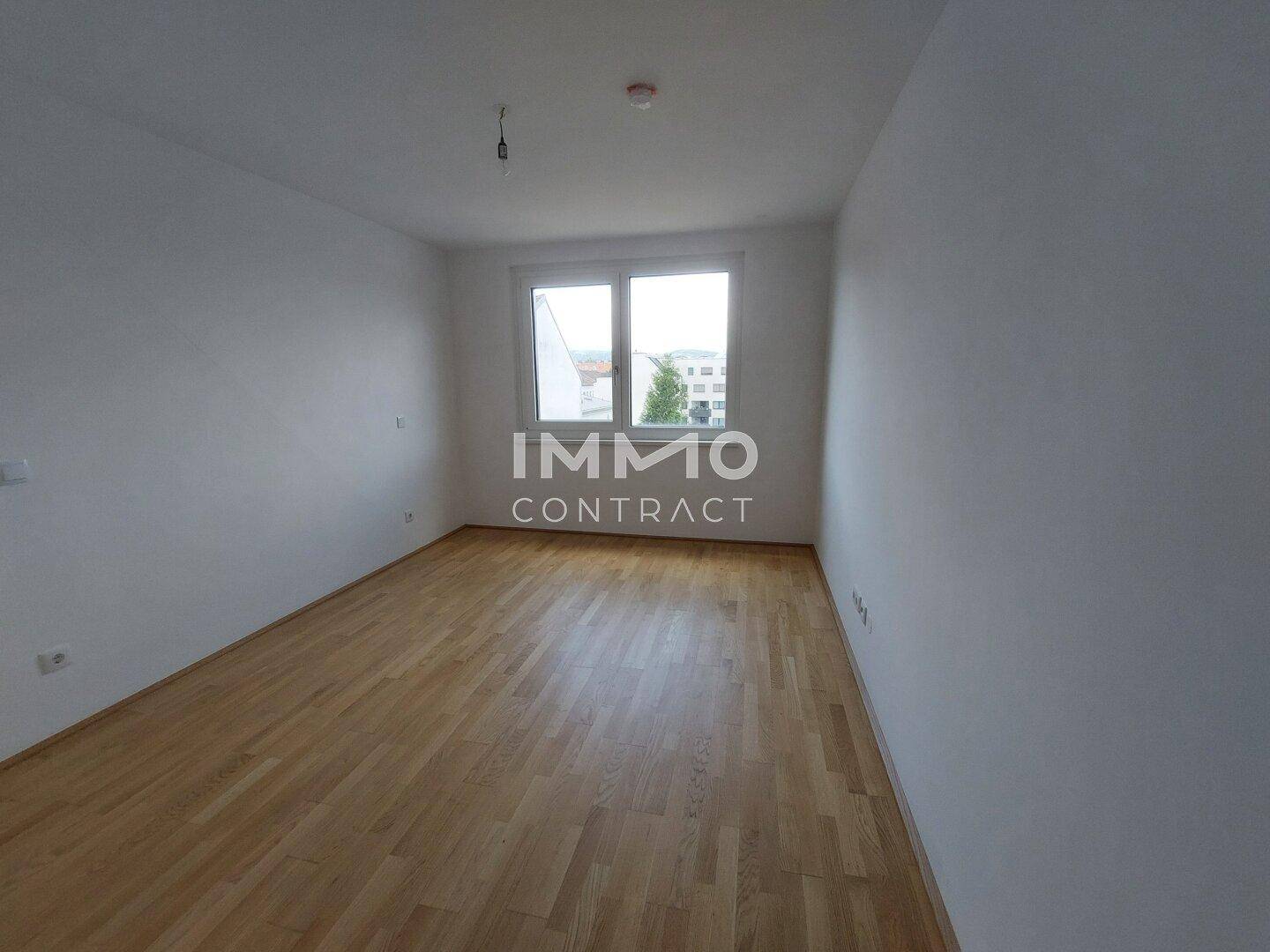 Heller, unmöblierter Raum mit Holzparkettboden und einem Fenster, das Tageslicht hereinlässt.