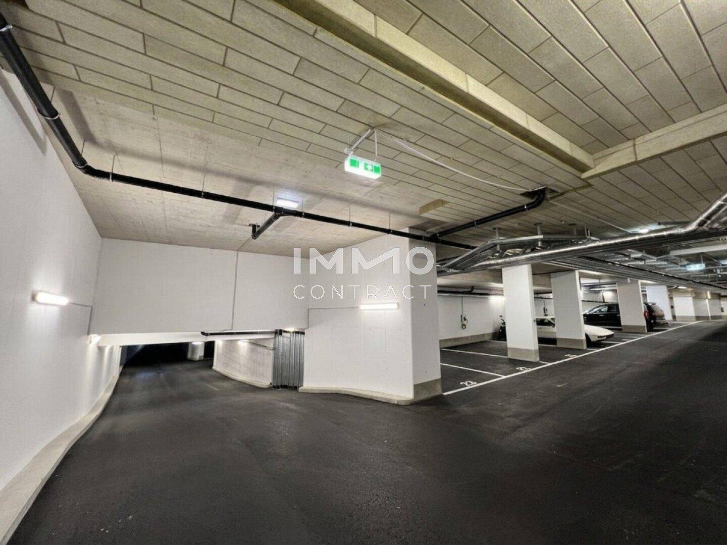 Geräumige Tiefgarage mit markierten Stellplätzen, Zufahrtsrampe und sichtbaren Installationen an der Decke.
