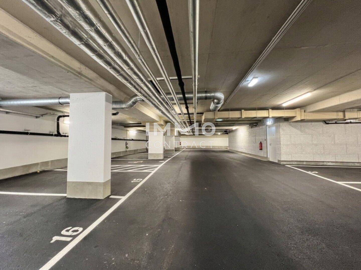 Geräumige Tiefgarage mit vielen Stellplätzen und sichtbaren Versorgungsleitungen an der Decke.