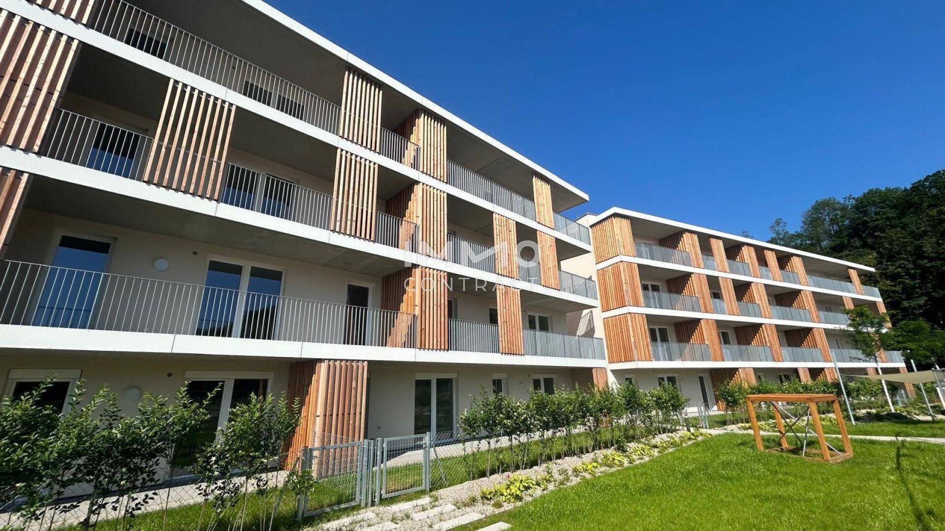 Mehrere moderne Wohngebäude mit Balkonen und Holzdetails, umgeben von einer grünen Rasenfläche.