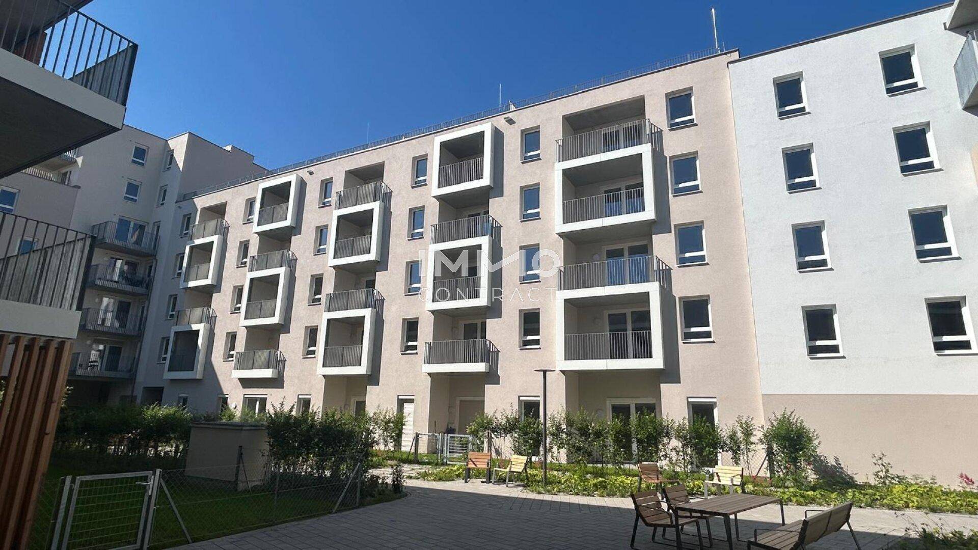 Fassade eines modernen Wohngebäudes mit quadratischen Balkonen und einem gemeinschaftlichen Innenhof mit Sitzgelegenheiten.
