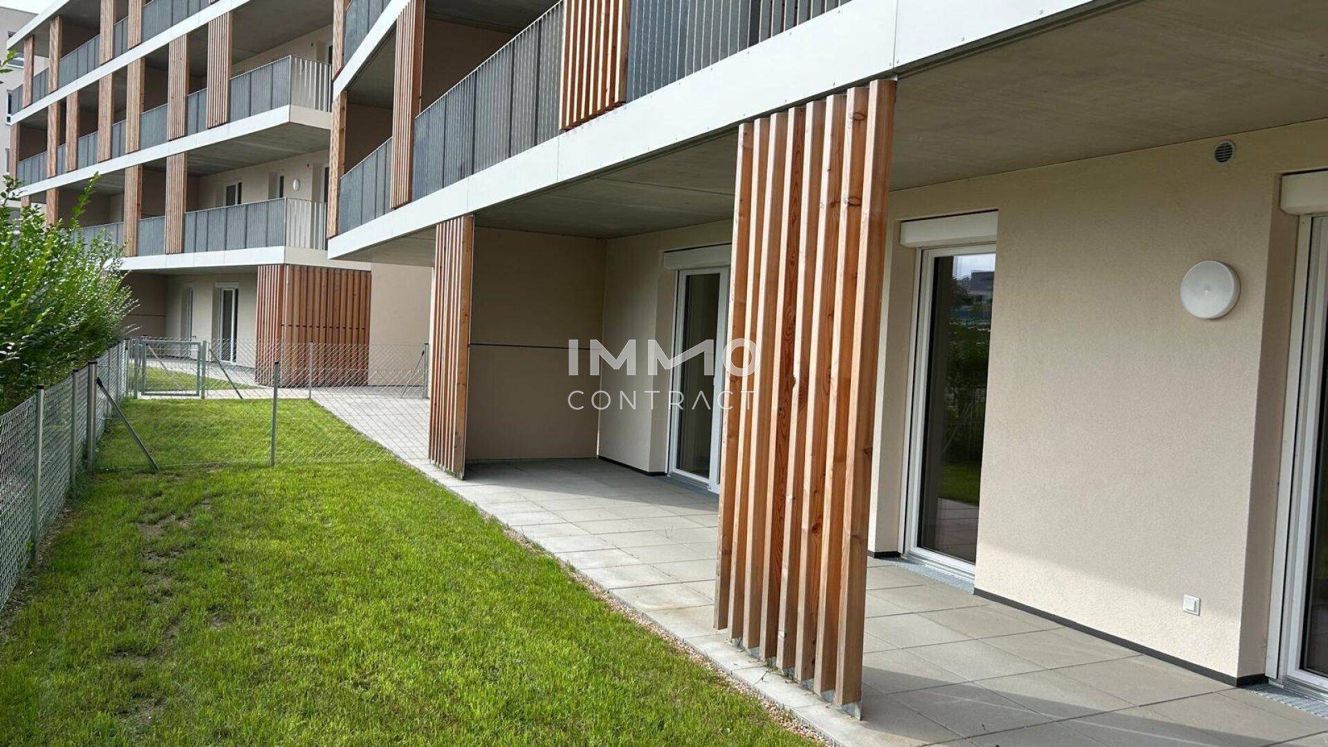 Ebenerdige Terrasse mit Steinplatten und Holzelementen, angrenzend an eine Rasenfläche.