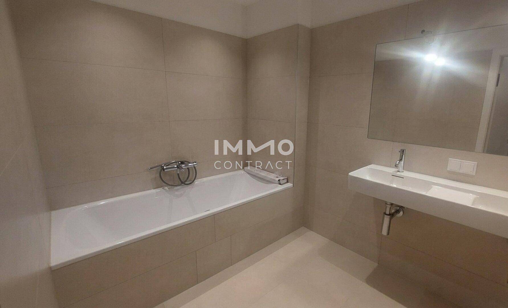 Modernes Badezimmer mit hellen Fliesen, einer Badewanne und einem wandmontierten Waschbecken.