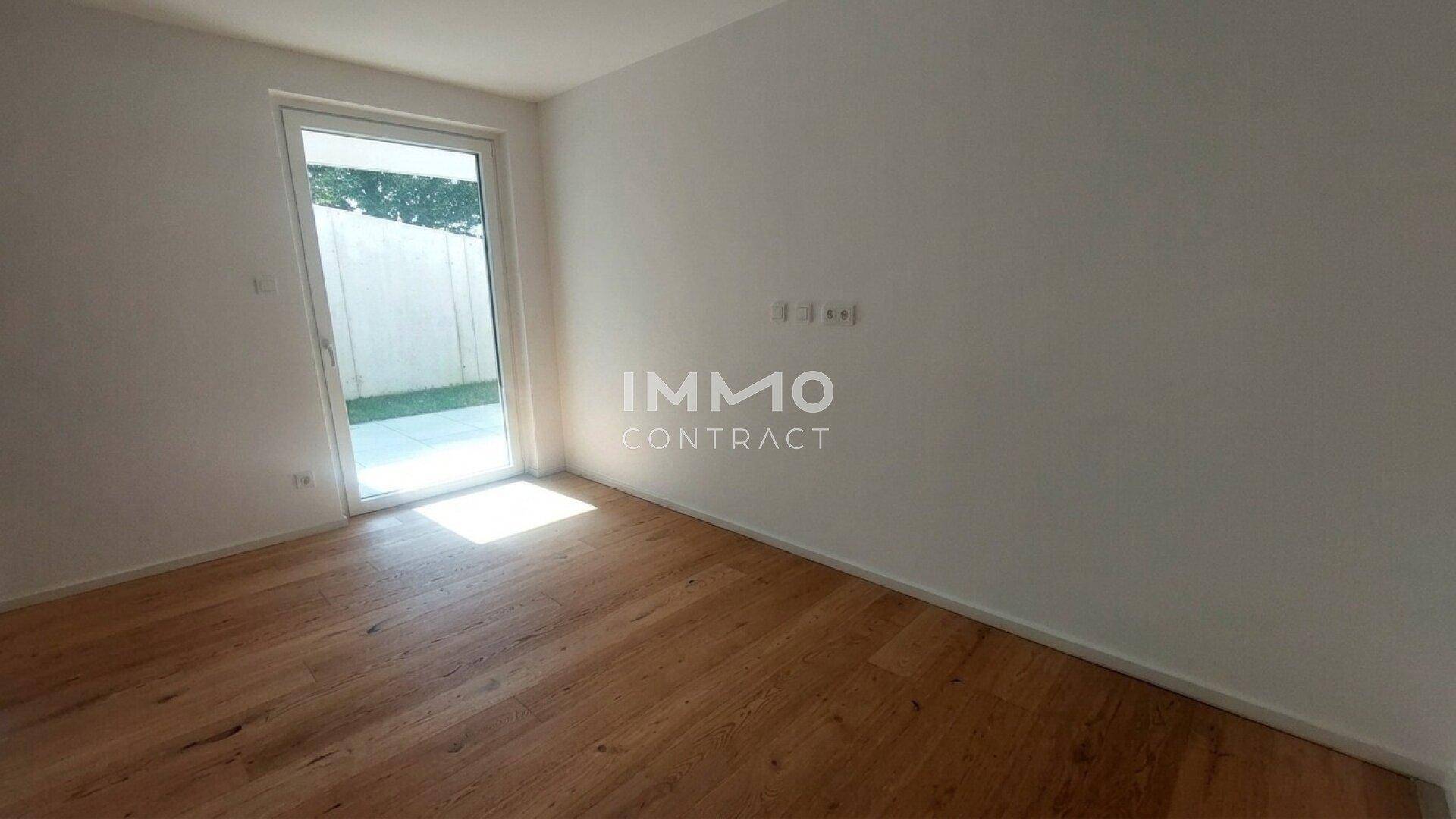 Leeres Zimmer mit Holzboden und direktem Zugang zu einem kleinen, gepflasterten Außenbereich.
