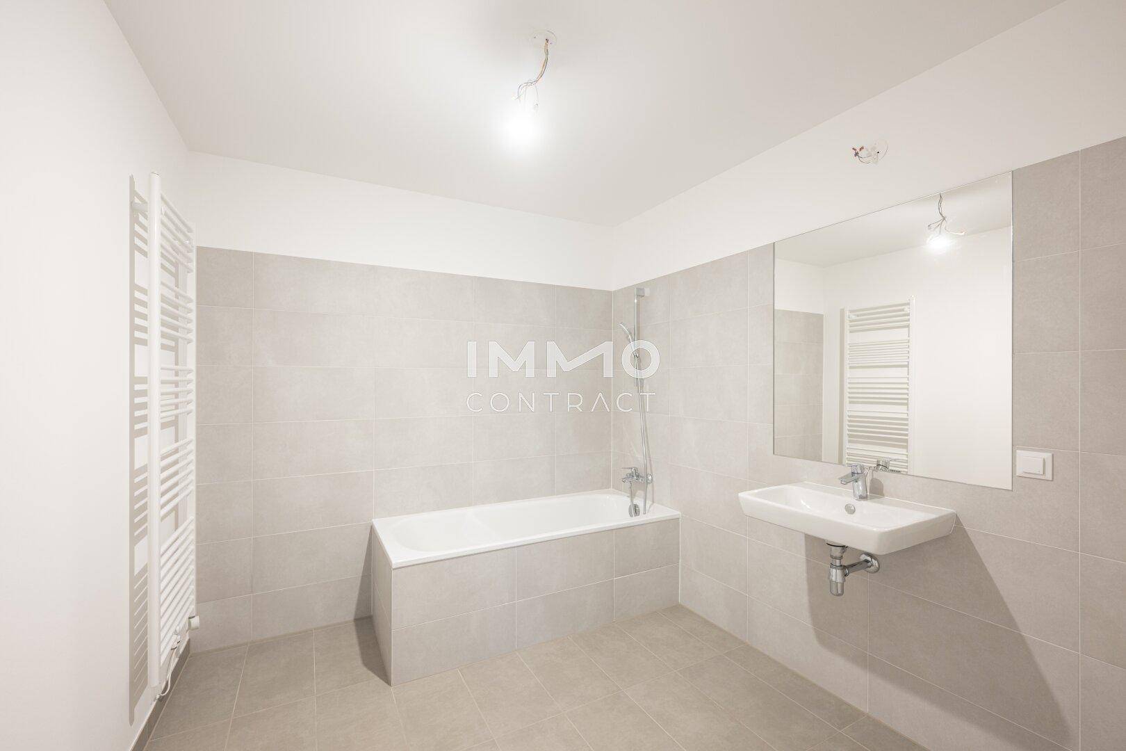 Modernes Badezimmer mit Badewanne, Waschbecken, großem Spiegel und beheiztem Handtuchhalter.