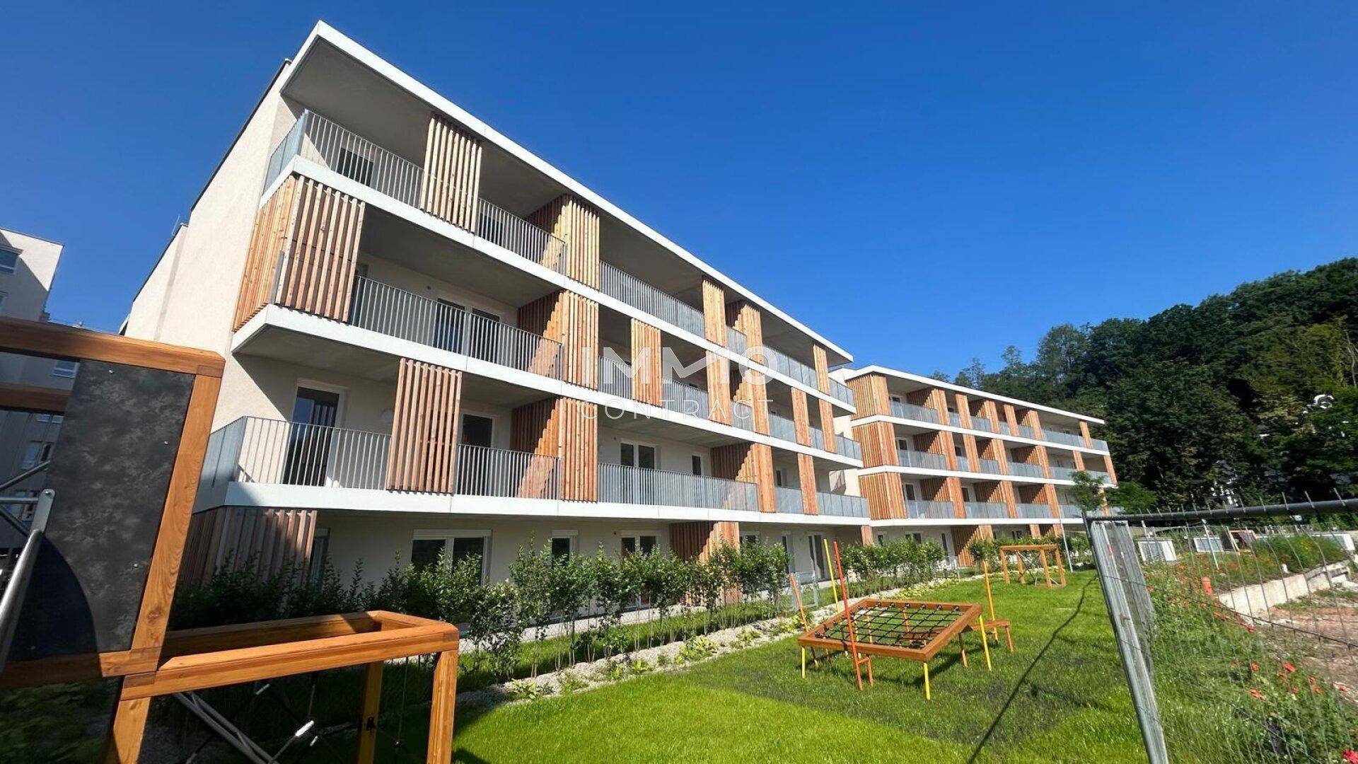 Zwei moderne Wohngebäude mit Balkonen und einem Spielplatz im Außenbereich unter blauem Himmel.
