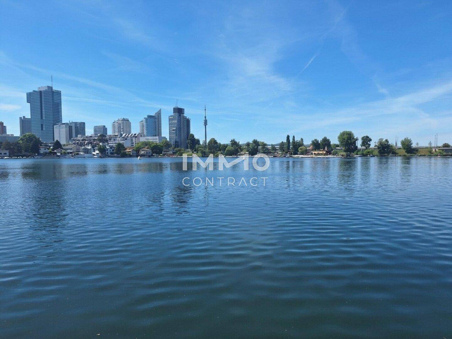 Panoramablick über einen See mit moderner Skyline im Hintergrund unter strahlend blauem Himmel.