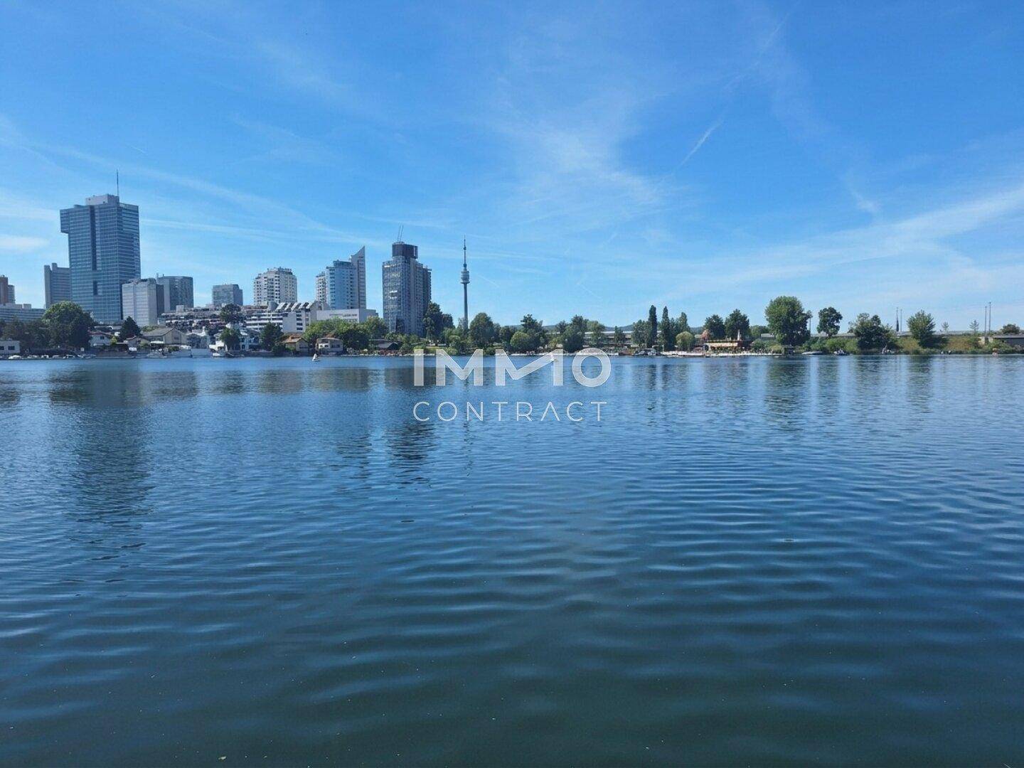 Panoramablick über den See mit der beeindruckenden Skyline der Stadt im Hintergrund unter blauem Himmel.