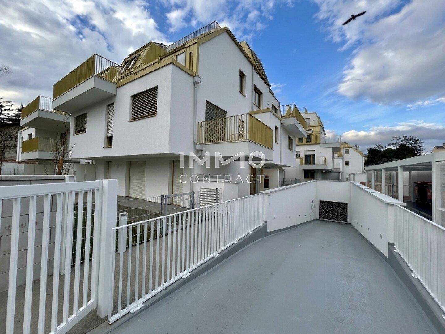 Moderne Wohnanlage mit weißer Fassade, Balkonen und Zufahrt zur Tiefgarage.