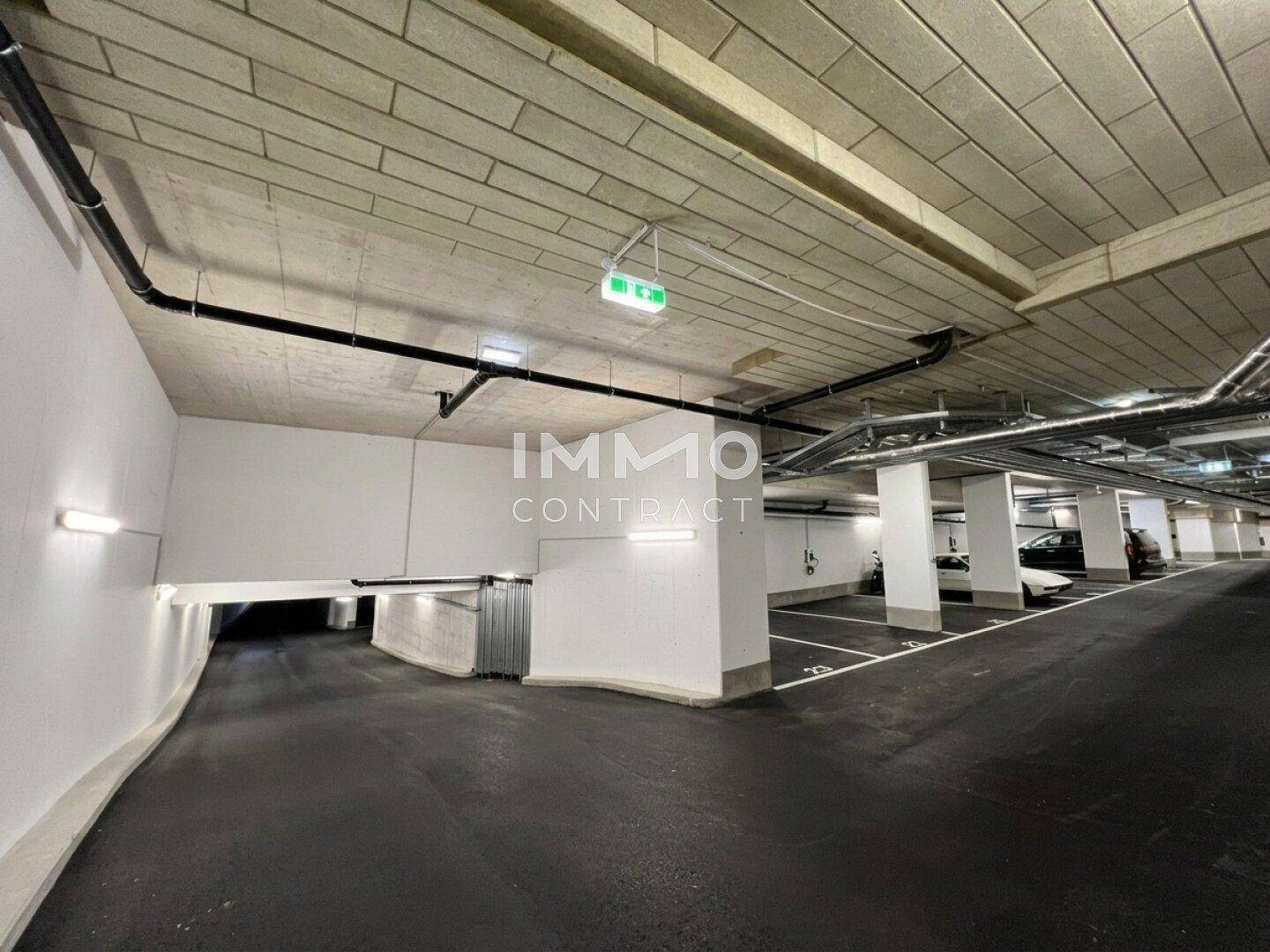 Tiefgarage mit markierten Stellplätzen, Betonwänden und sichtbaren Installationen.