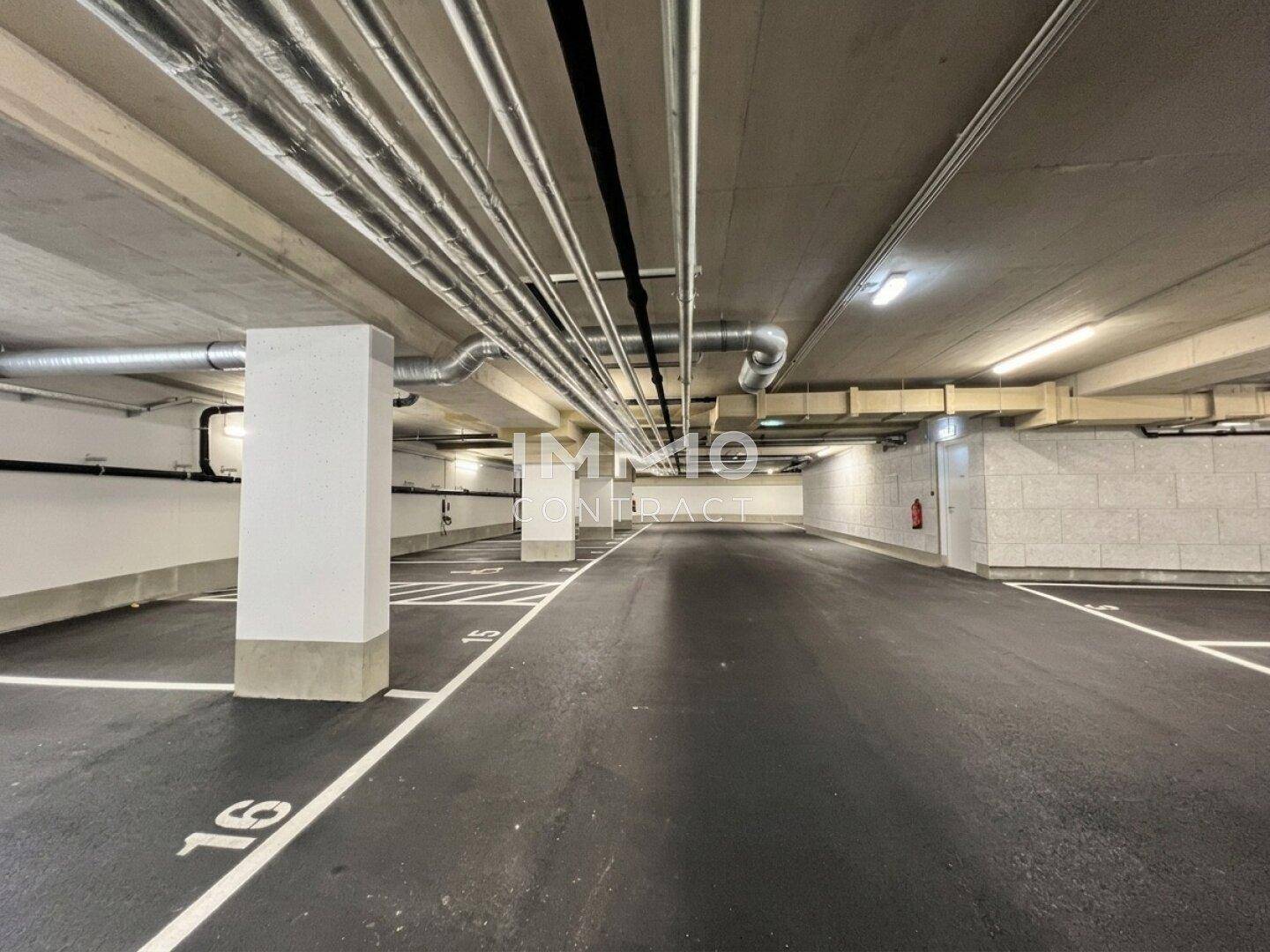 Geräumige Tiefgarage mit markierten Stellplätzen und sichtbaren Installationen an der Decke.