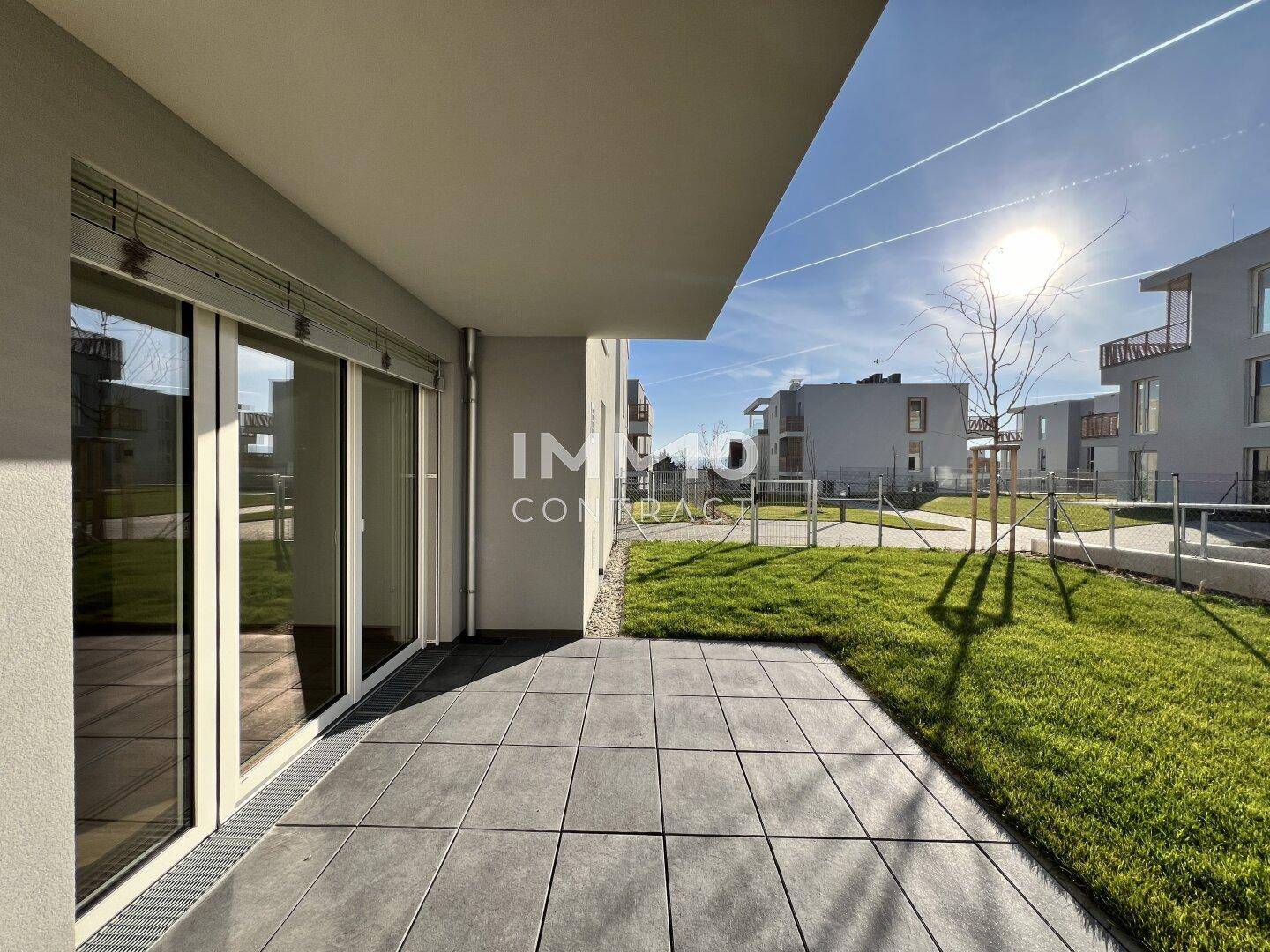 Helle Terrasse mit grauen Fliesen und Zugang zum Gartenbereich, ideal für entspannte Stunden im Freien.