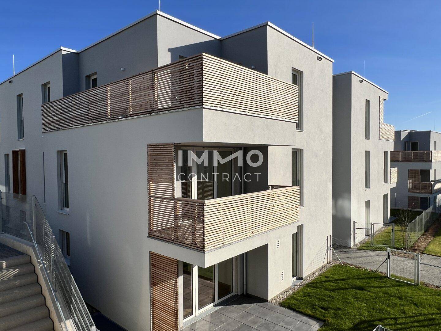 Eckansicht eines modernen Apartmentgebäudes mit mehreren Balkonen und Holzlamellen als Geländer.