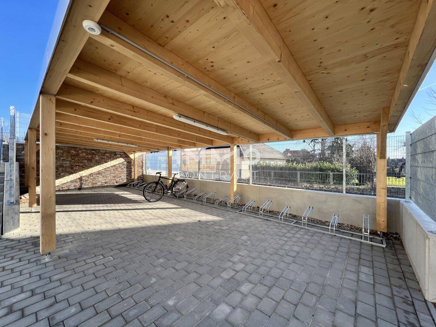 Überdachter Fahrradabstellplatz mit Holzkonstruktion und gepflastertem Boden, bietet Schutz für Fahrräder.