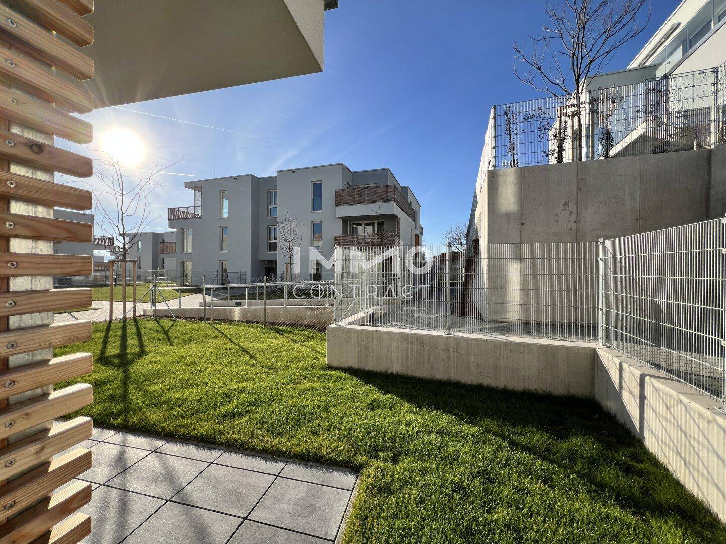 Sonniger Terrassenbereich mit Fliesenboden und Blick auf die umliegende Grünanlage und Gebäude.