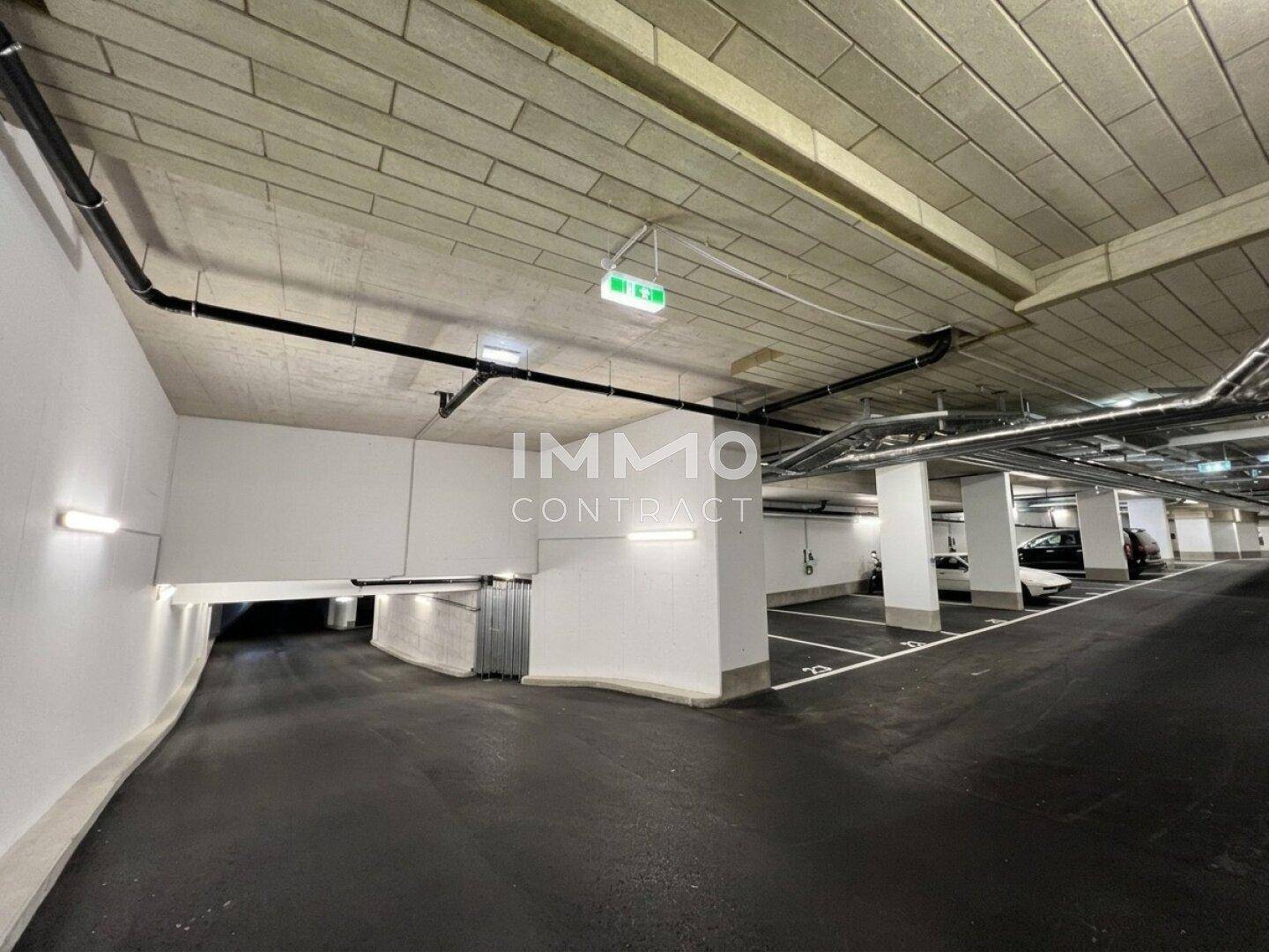 Moderne Tiefgarage mit zahlreichen Stellplätzen, Zufahrtsrampe und sichtbaren Installationen an der Decke.