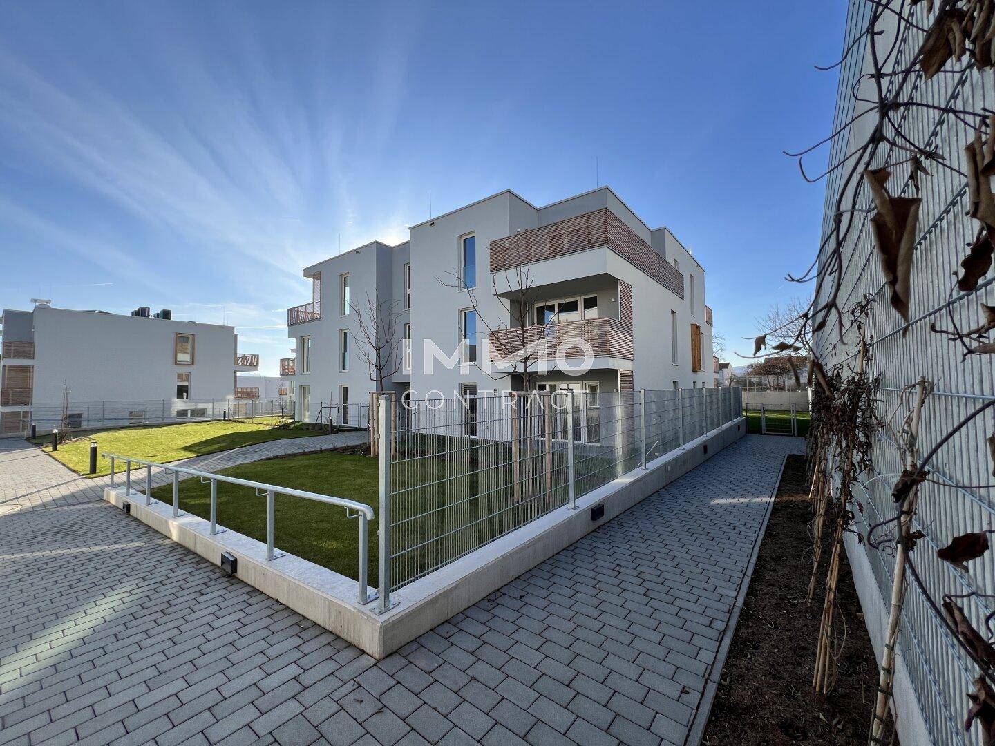 Neubau-Wohngebäude mit moderner Architektur, Balkonen und umzäunten Grünflächen unter blauem Himmel.
